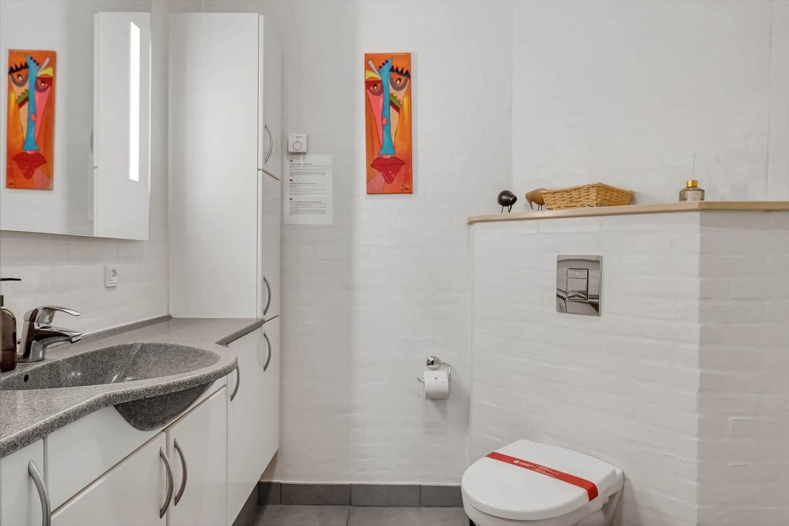 Badezimmer mit Waschbecken, Toilette und Wandbildern.