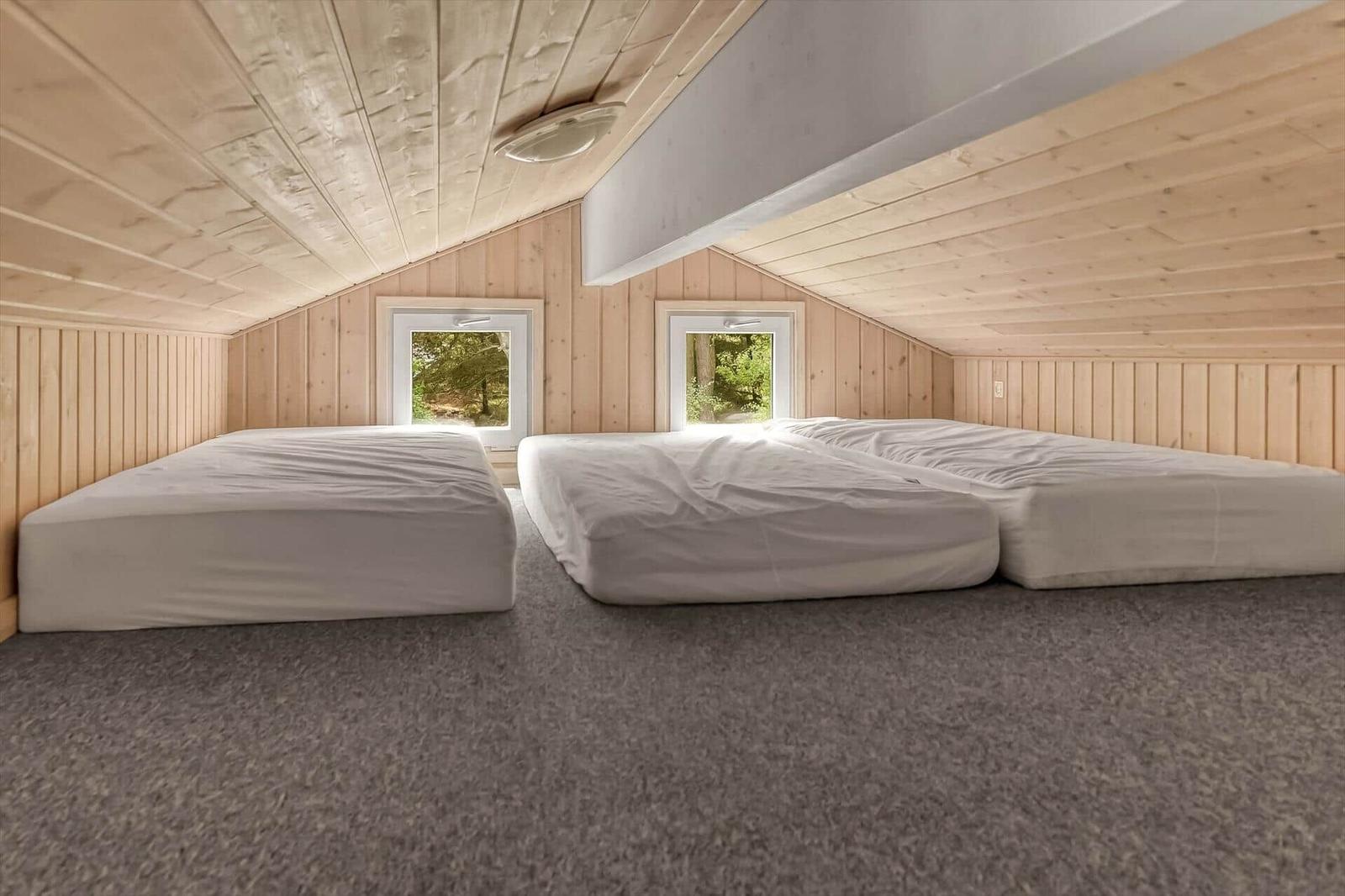 Drei Matratzen auf dem Boden in einem Holzhaus mit zwei Fenstern und Holzwänden.