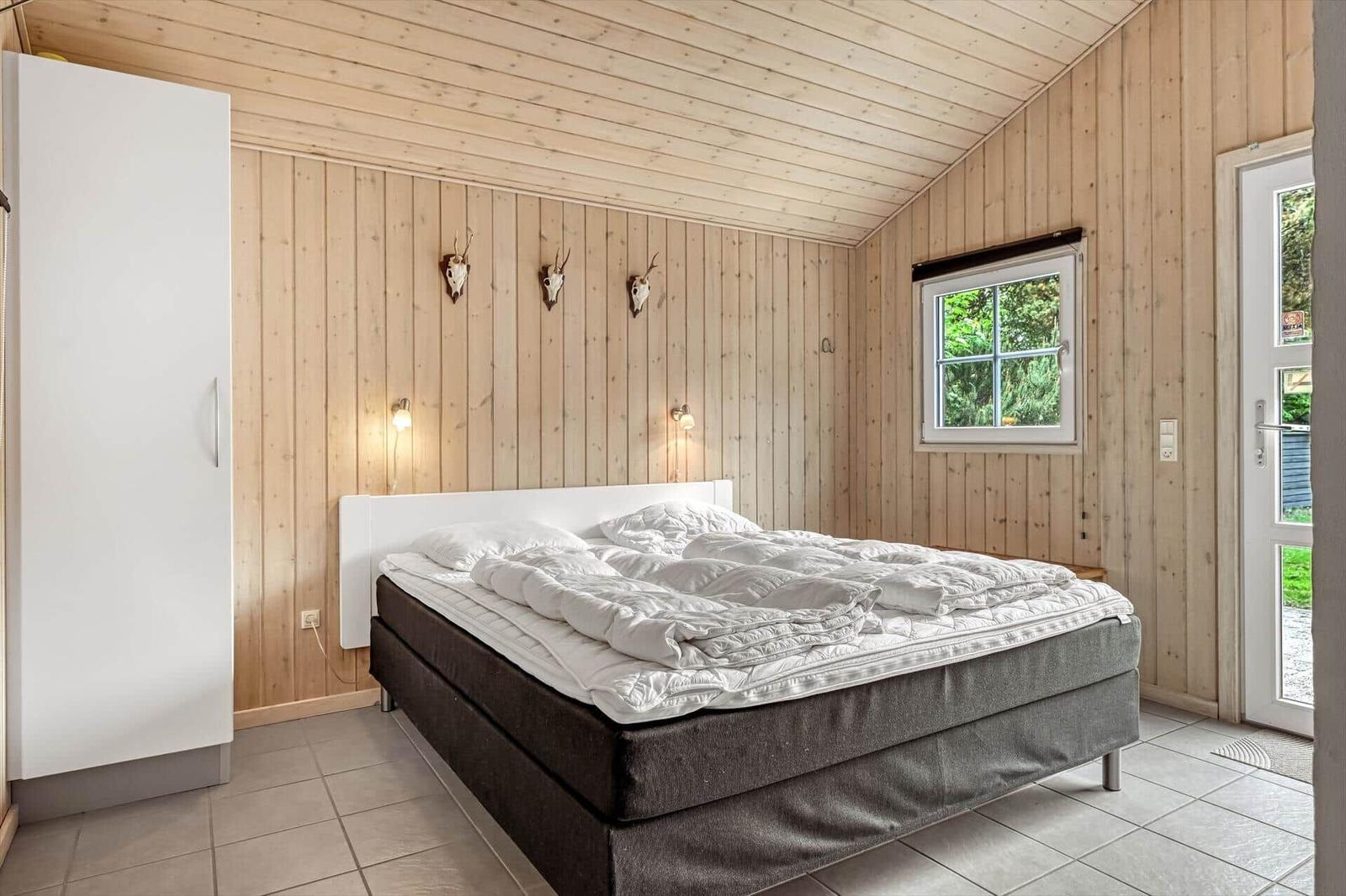 Schlafzimmer mit Holzwand, Bett, Fenster und Tür.