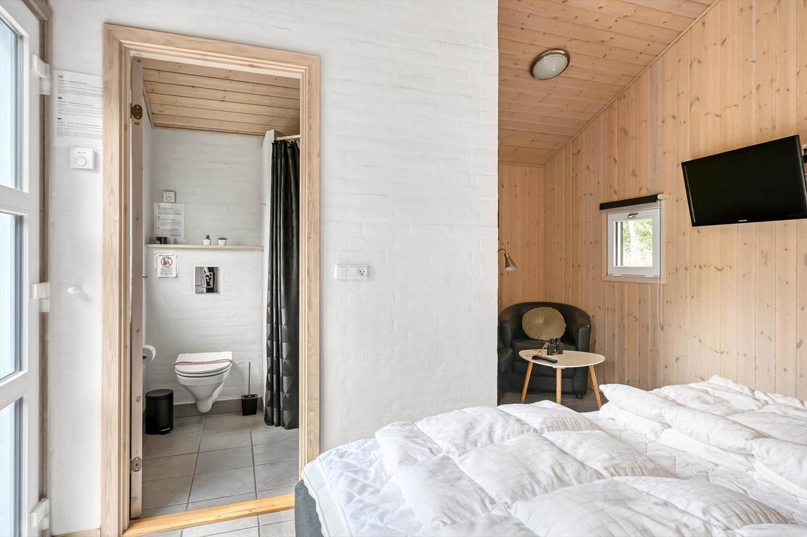 Schlafzimmer mit Bett, Fernseher und Sitzgelegenheit. Nebenraum mit Toilette und Dusche.