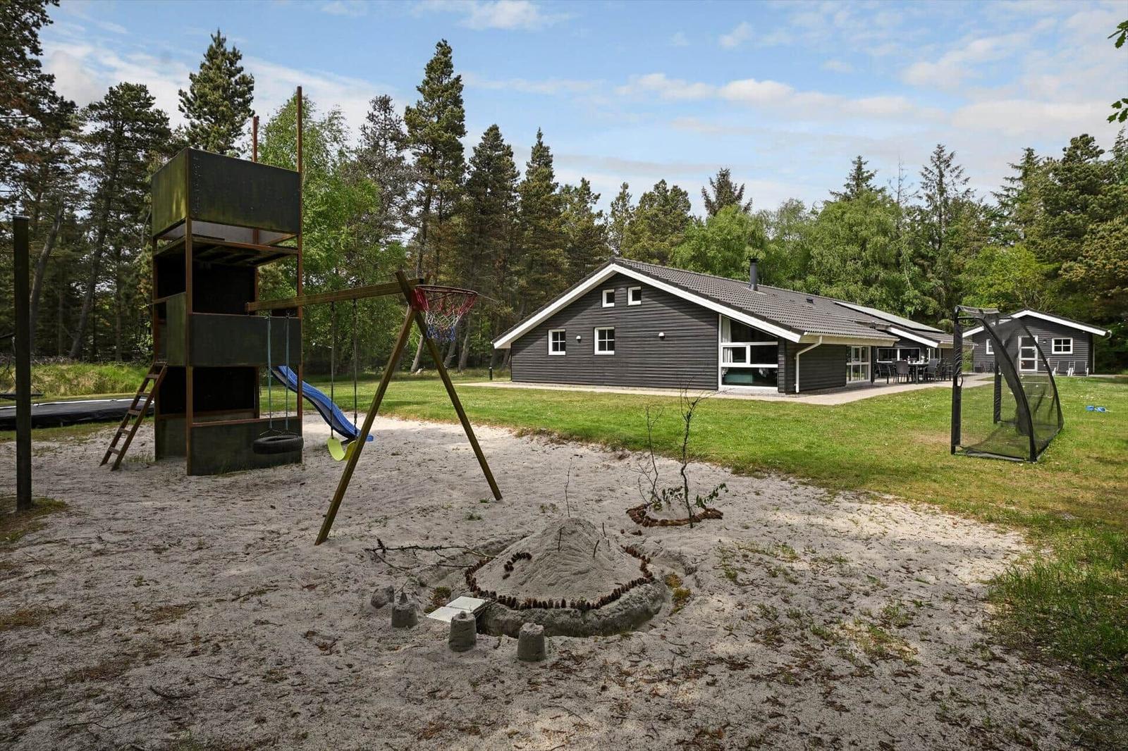Ein Ferienhaus mit Spielplatz, Sandkasten und Grünfläche im Wald.