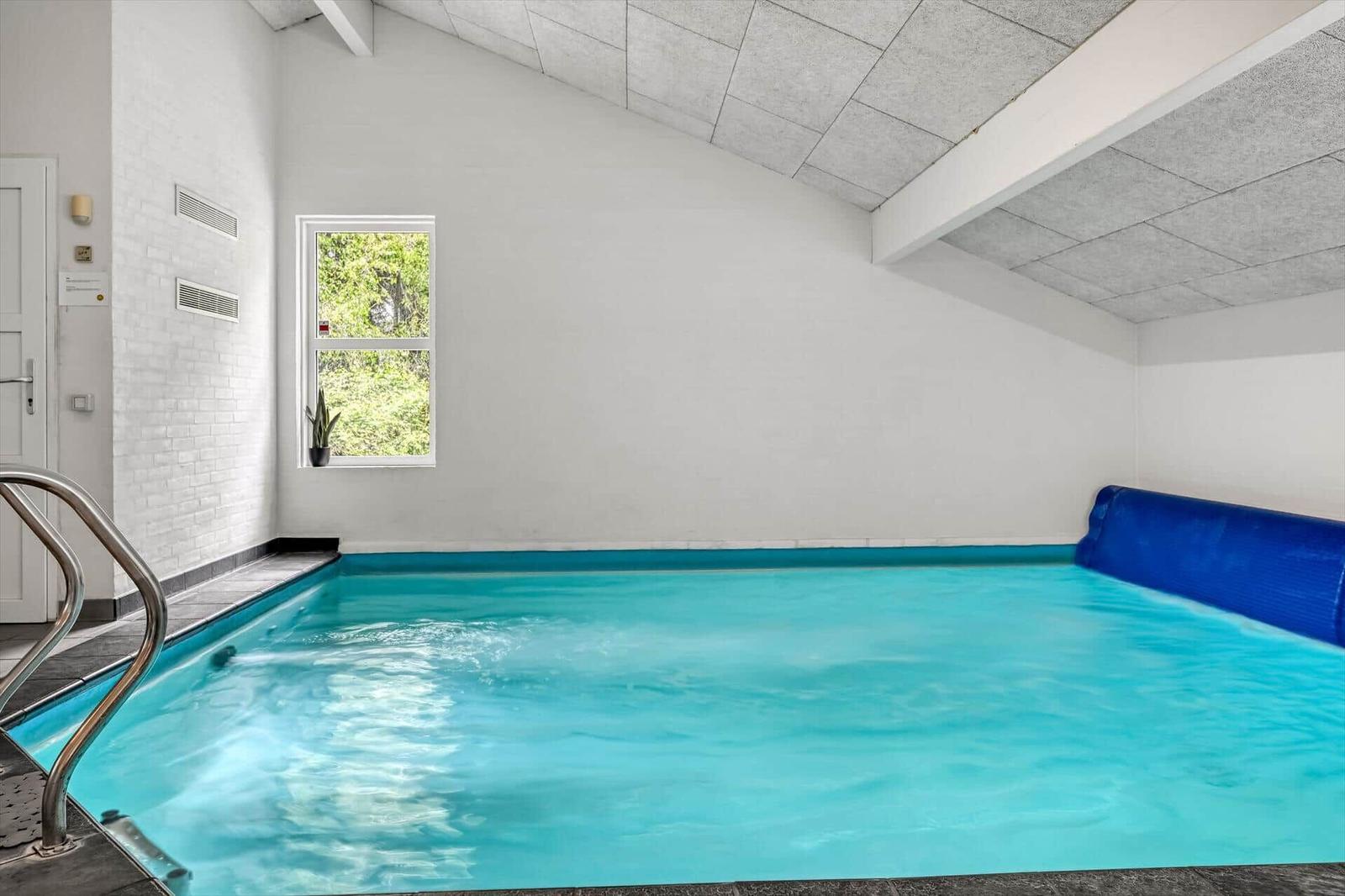 Innere Schwimmhalle mit blauem Wasser und Fenster zur Natur.