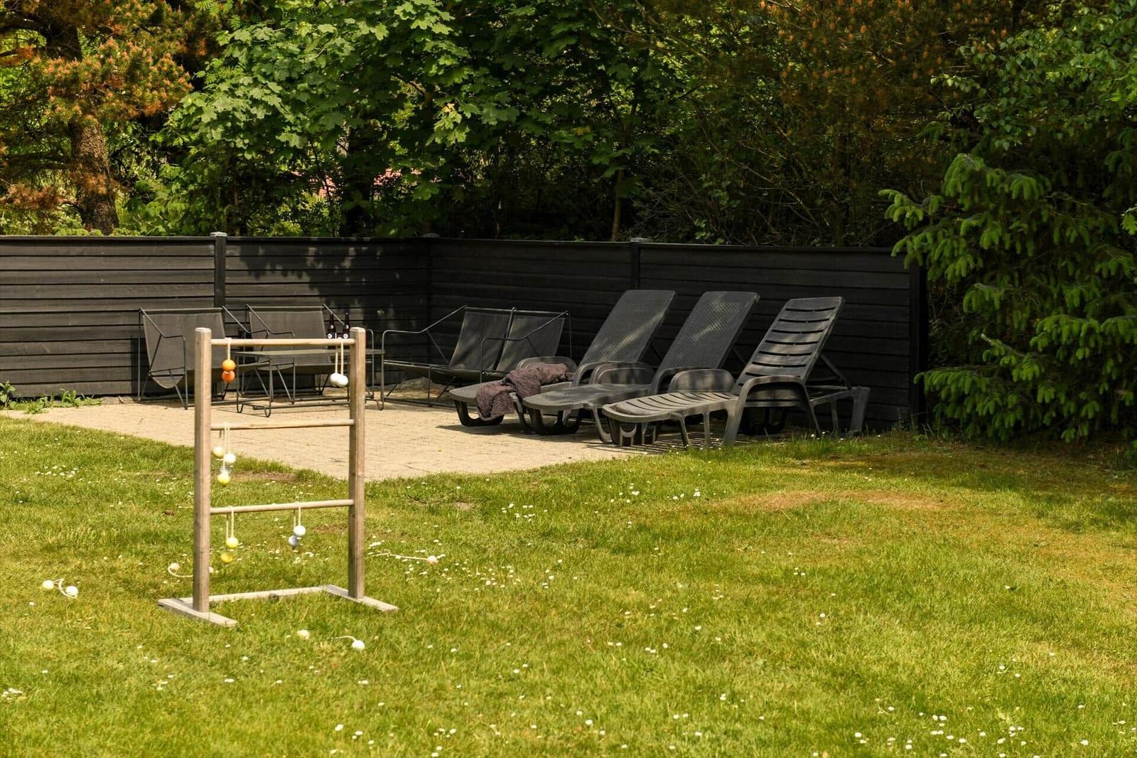 Garten mit Liegestühlen und Spielgerät vor dunklem Holzzaun.