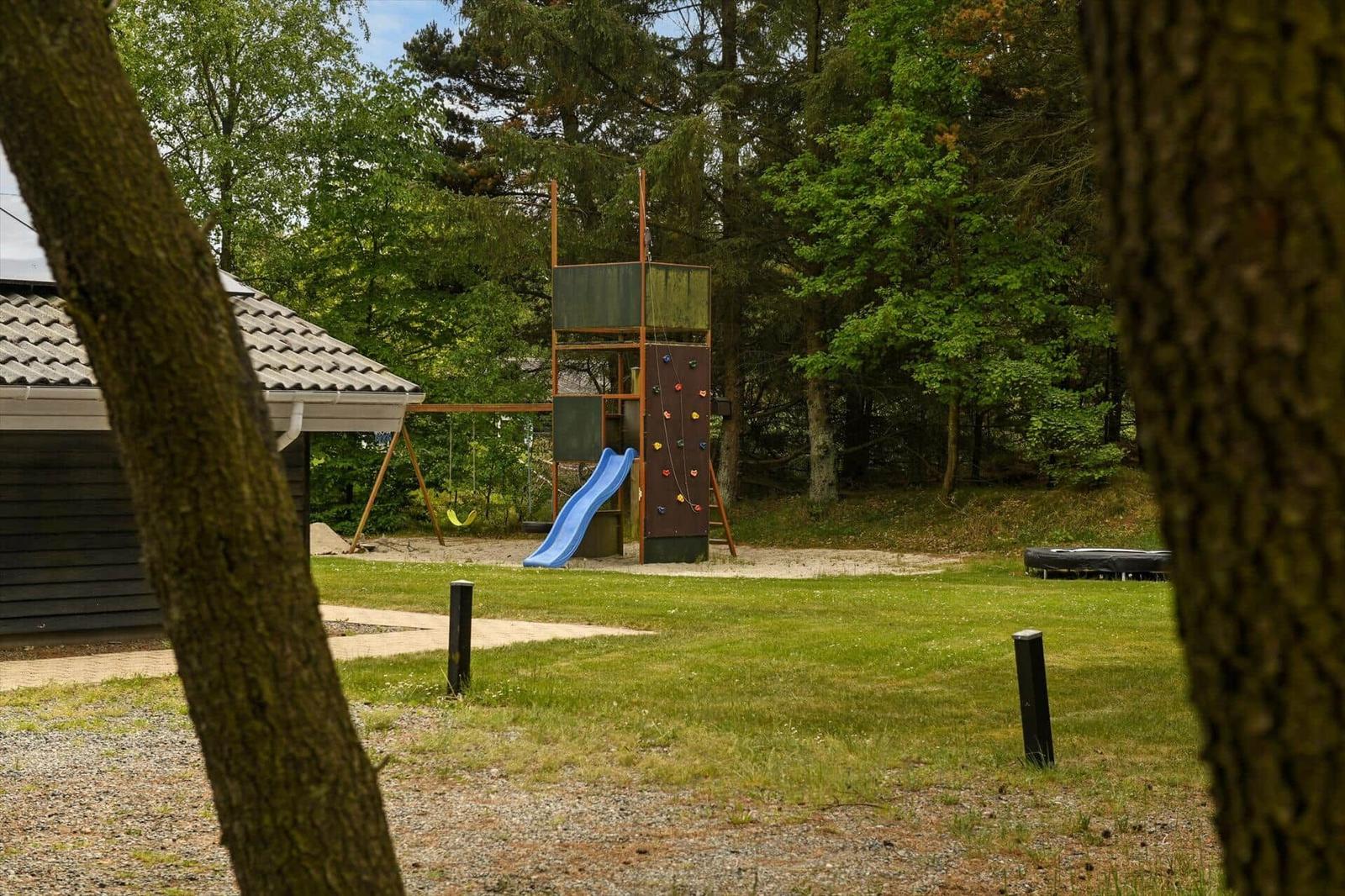 Hinterhof mit Spielplatz, Rutsche und Kletterwand. Grasfläche und Wald im Hintergrund.