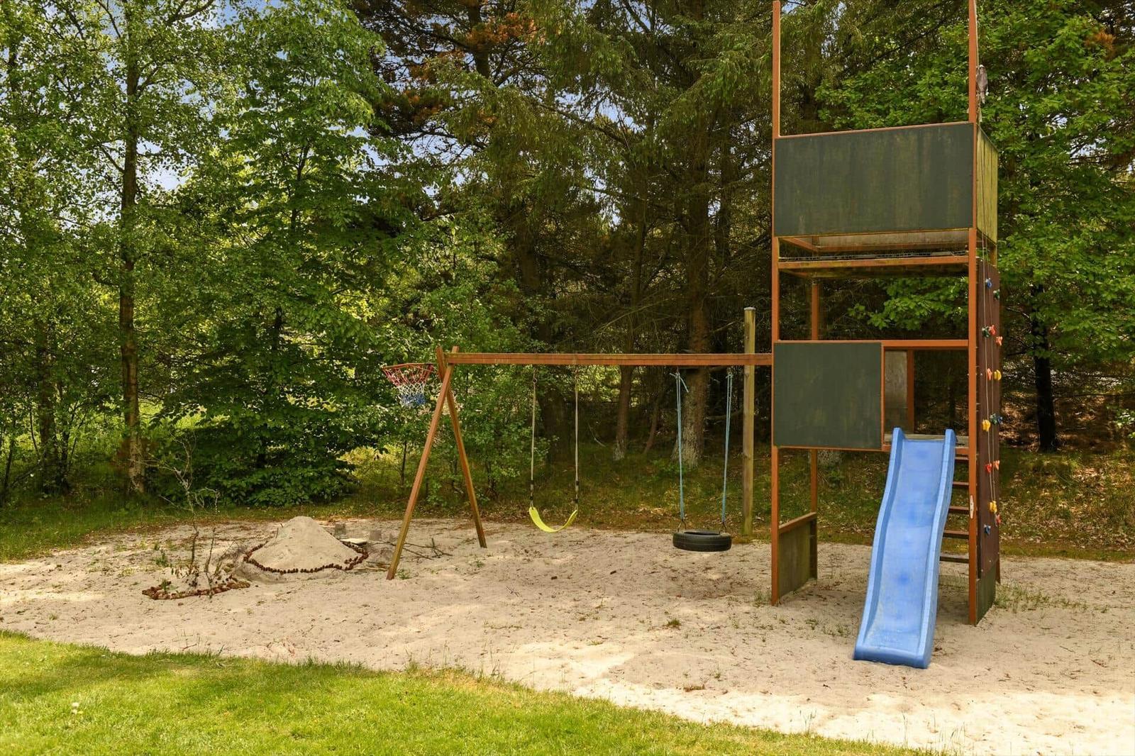 Kinderbereich mit Sandkasten, Rutsche und Kletterwand im Wald.