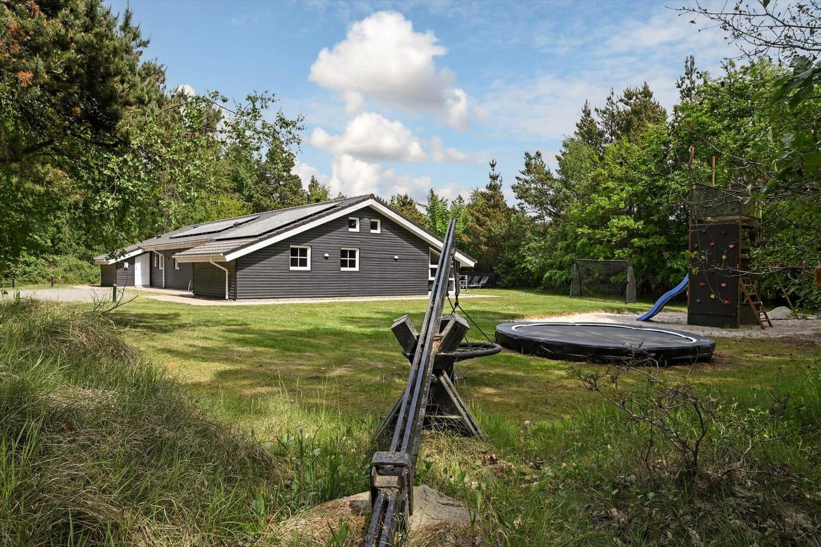 Ein graues Haus mit Spielplatz und Trampolin im Garten.