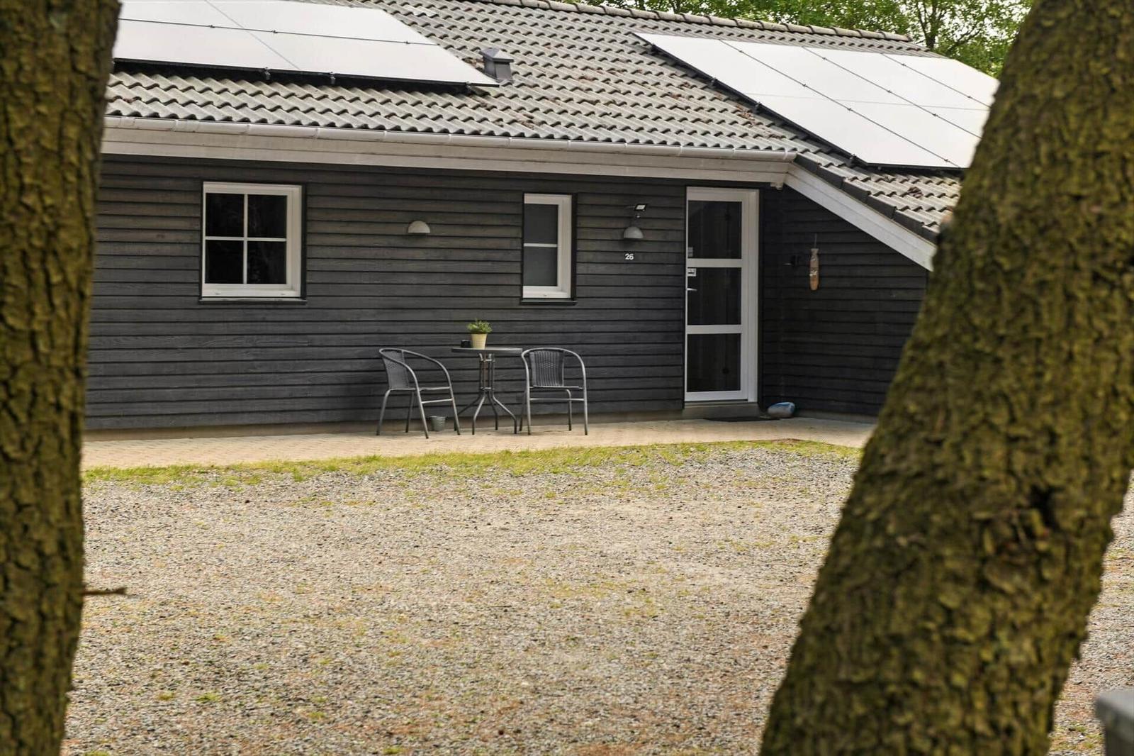 Ein dunkel verputztes Haus mit Solarpanelen, einer Terrasse und einem Garten.