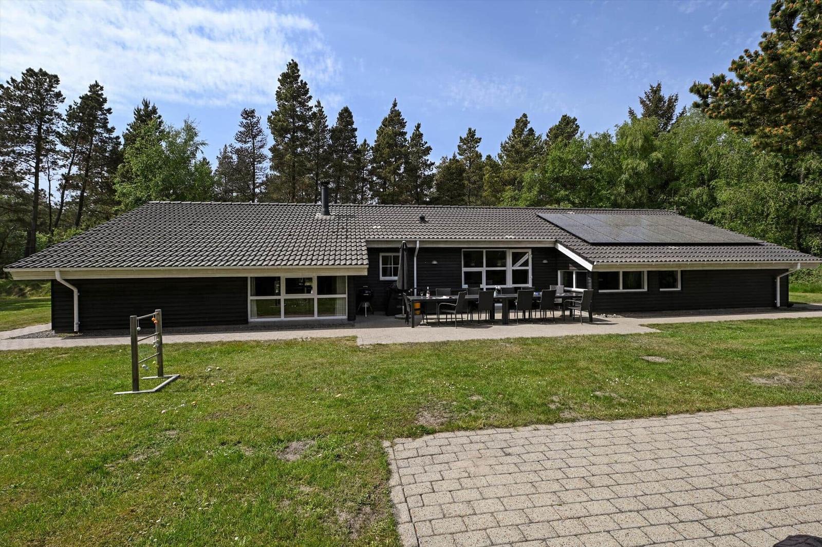 Ein modernes Haus mit Terrasse, Garten und Blick auf einen Wald.