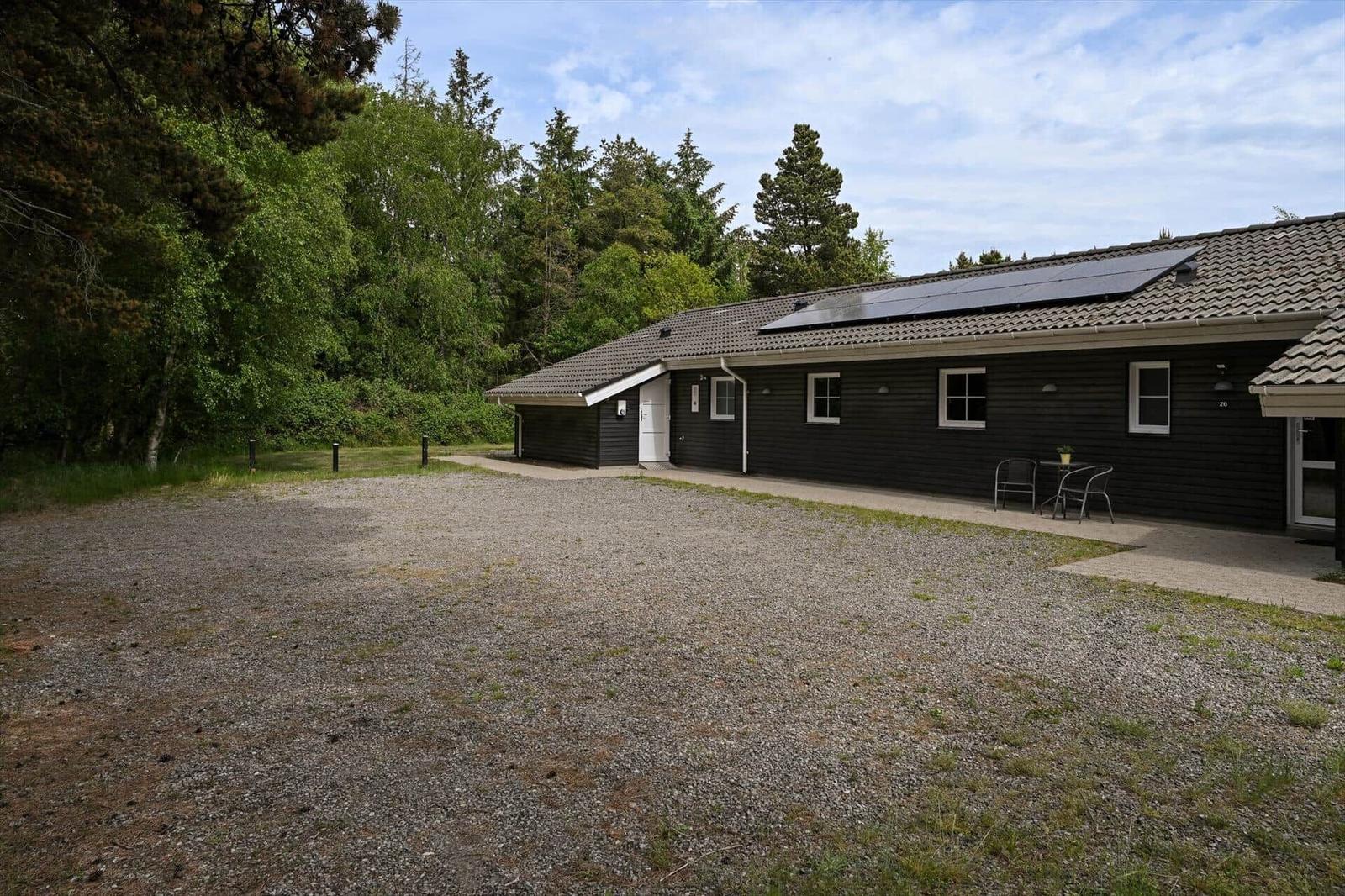 Schwarzes Holzhaus mit Solaranlage und Terrasse im Wald. Kiesfläche vor dem Gebäude.