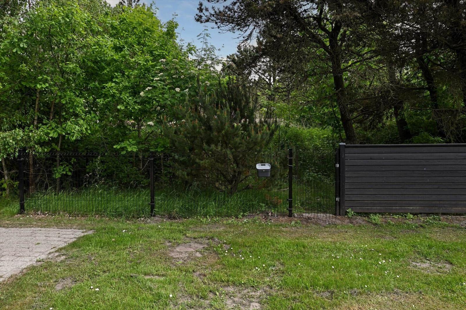 Gartenbereich mit Zaun, Grasfläche und Bäumen im Hintergrund.