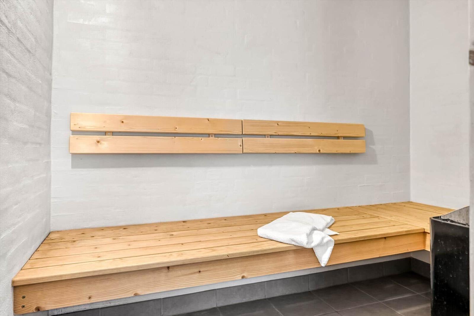 Holzbank mit Rückenlehne in Sauna mit weißer Wand und grauem Boden