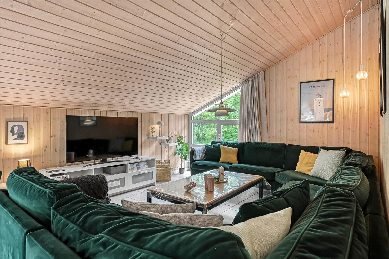 Wohnzimmer mit grünem Sofa, Fernseher und Holzwand.