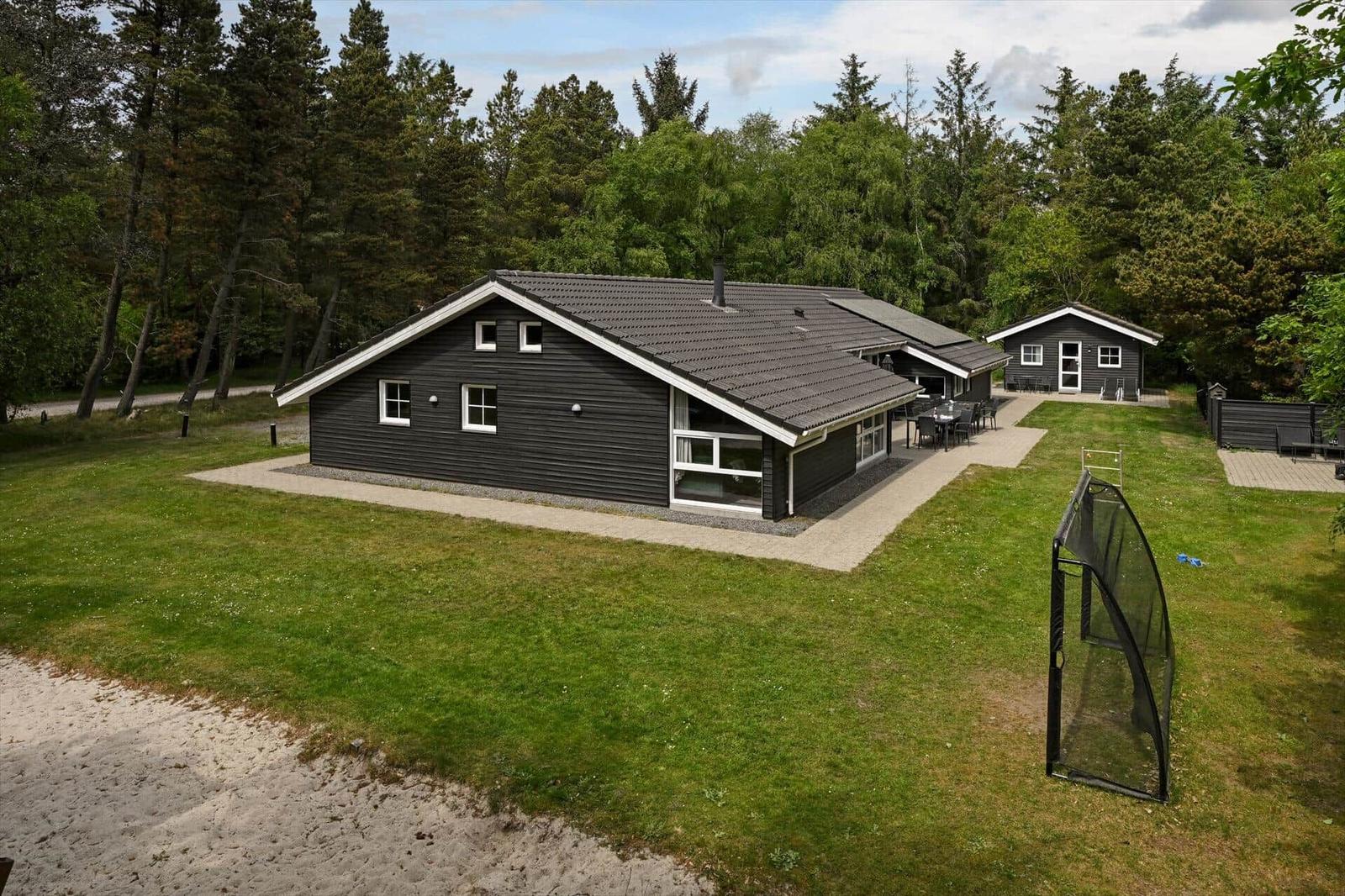 Schwarzes Ferienhaus mit Garten, Terrasse und Grillplatz. Umgeben von Wald und Sandstrand.
