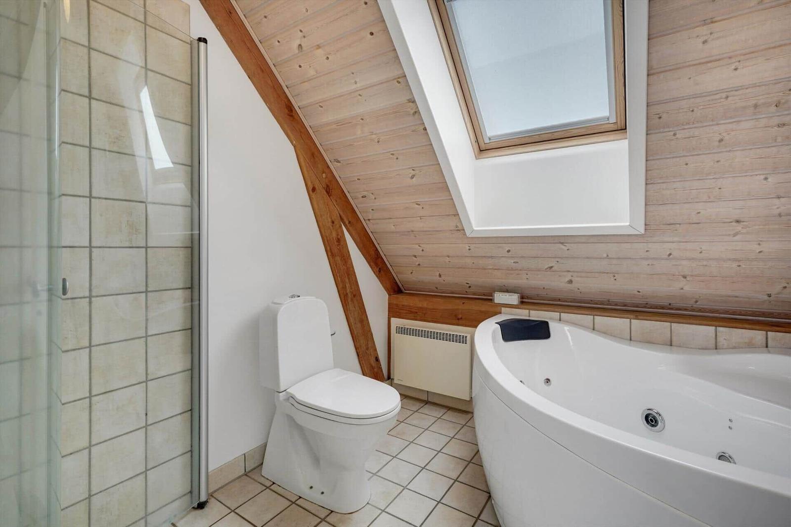Badezimmer mit Dusche, Toilette und Whirlpoolbad unter Holzdecke mit Dachfenster.