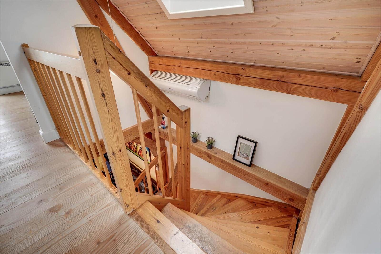 Holzgetreppe mit Geländer führt zur oberen Etage. Decke und Wände sind weiß.