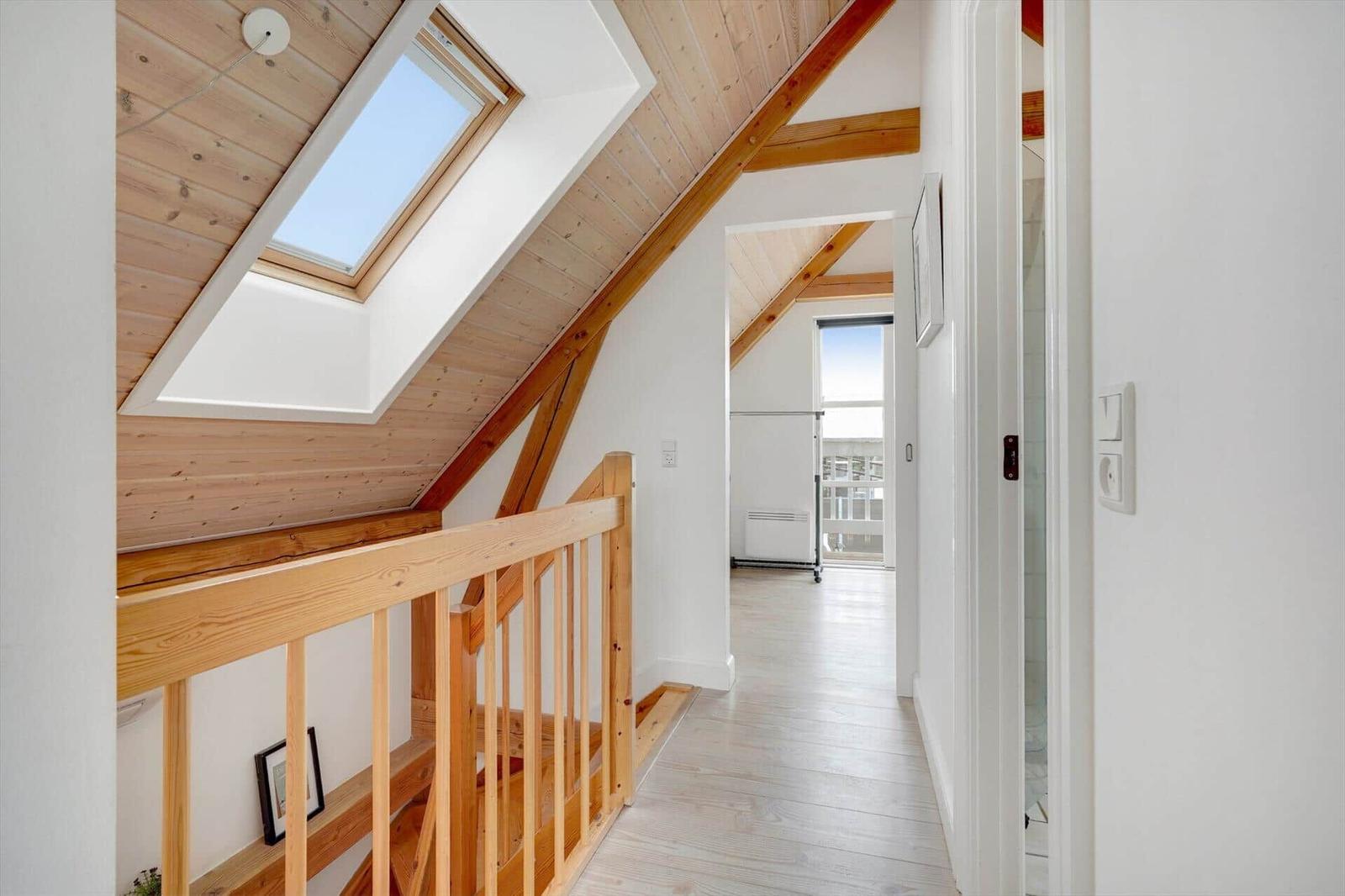Haus mit Holzdecke, Dachfenster und Holzgeländer. Blick in einen Flur mit weißen Wänden.