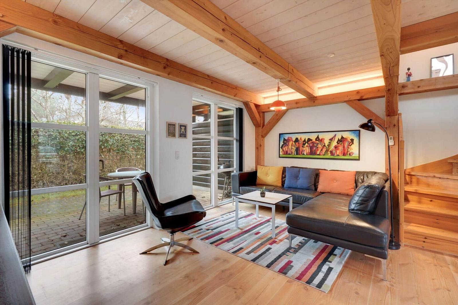 Wohnzimmer mit Ledersofa, Glasfront und Holzbalkendecke.