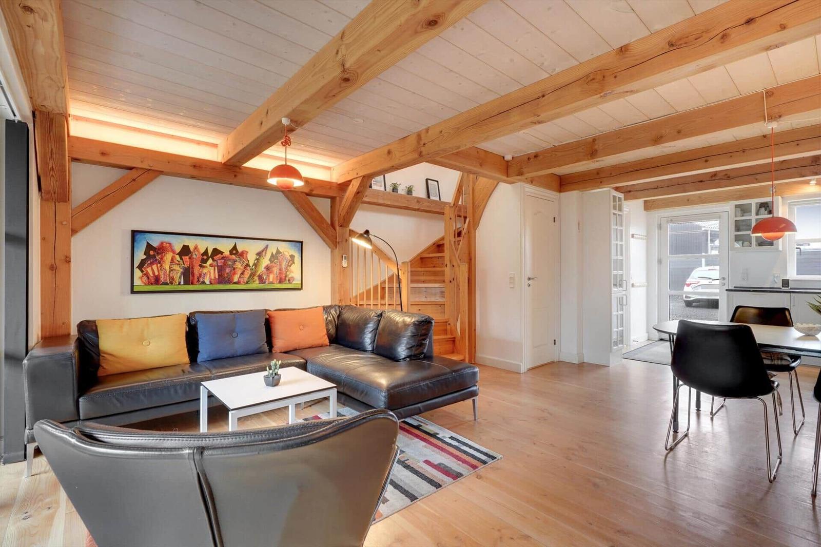 Wohn- und Essbereich mit Holzdecke, Sofa und Tisch. Treppenhaus im Hintergrund.