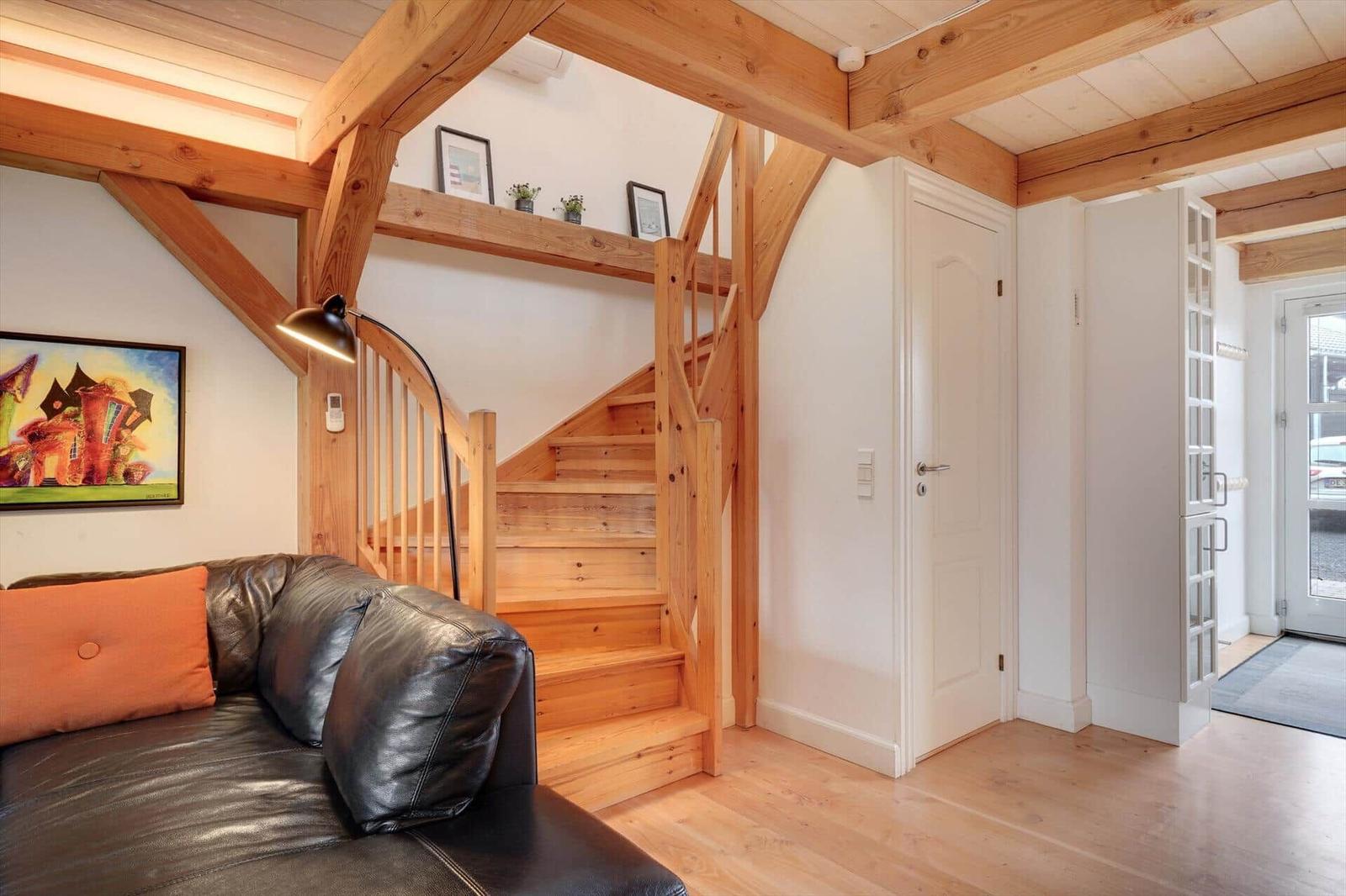 Wohnbereich mit Holztreppe, Sofa und Deckenbalken.