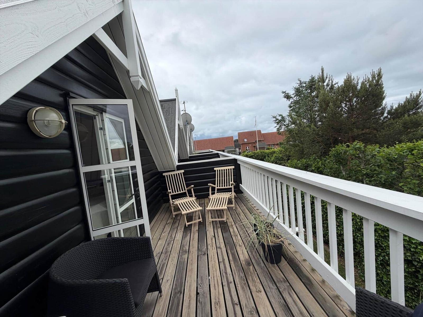 Terrasse mit Holzdielen, zwei Stühlen und weißer Brüstung. Blick auf Bäume und Häuser.