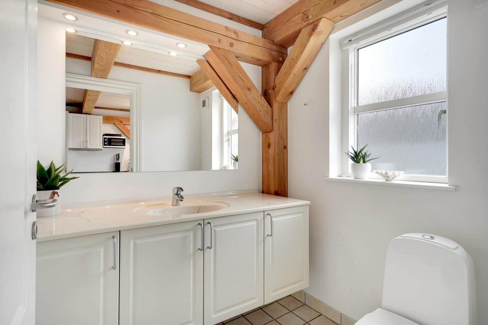 Badezimmer mit Waschbecken, Spiegel und Fenster. Holzbalken an der Decke.