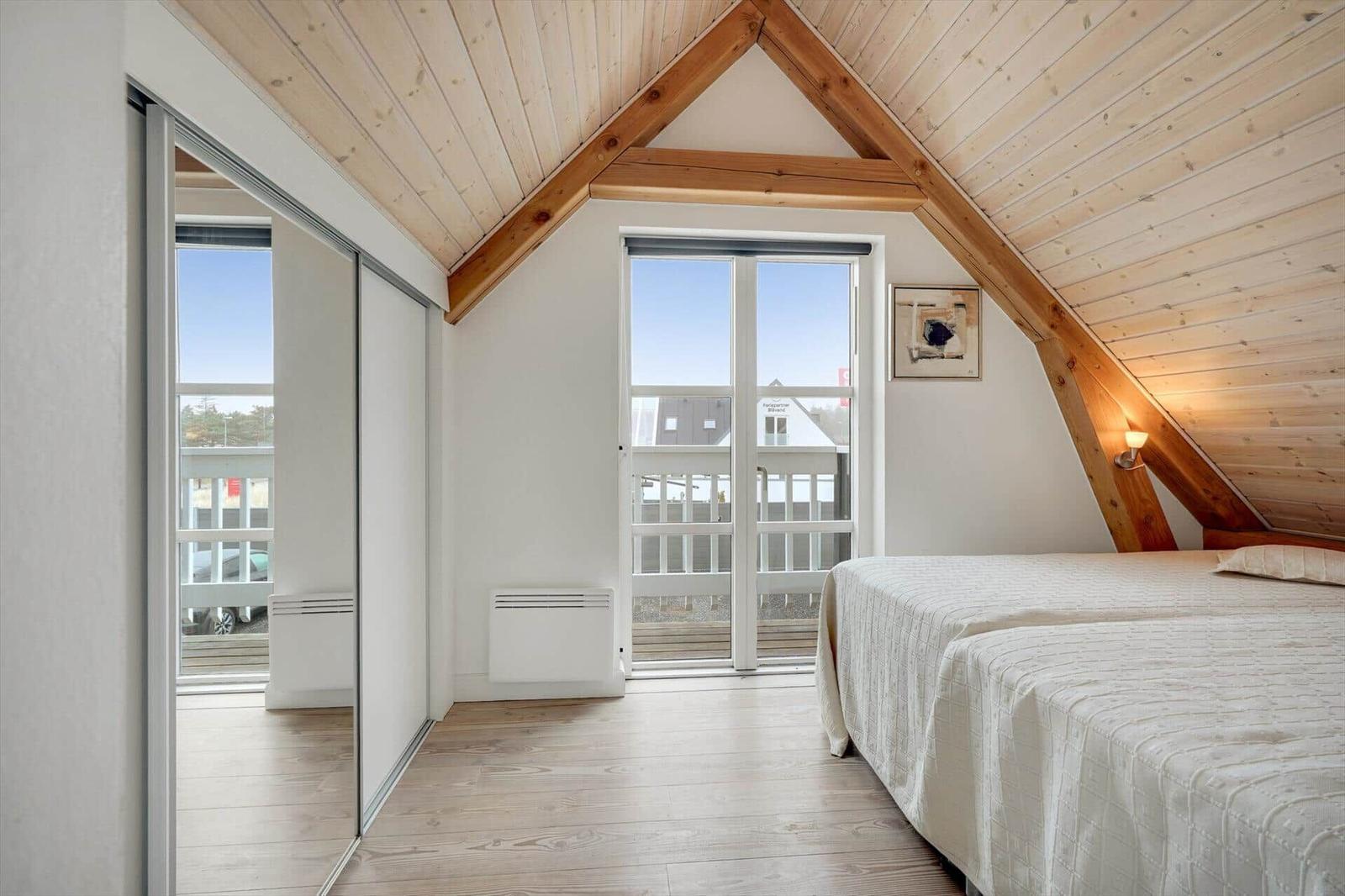 Schlafzimmer mit Dachschrägen, Holzboden und Fenster zum Balkon.