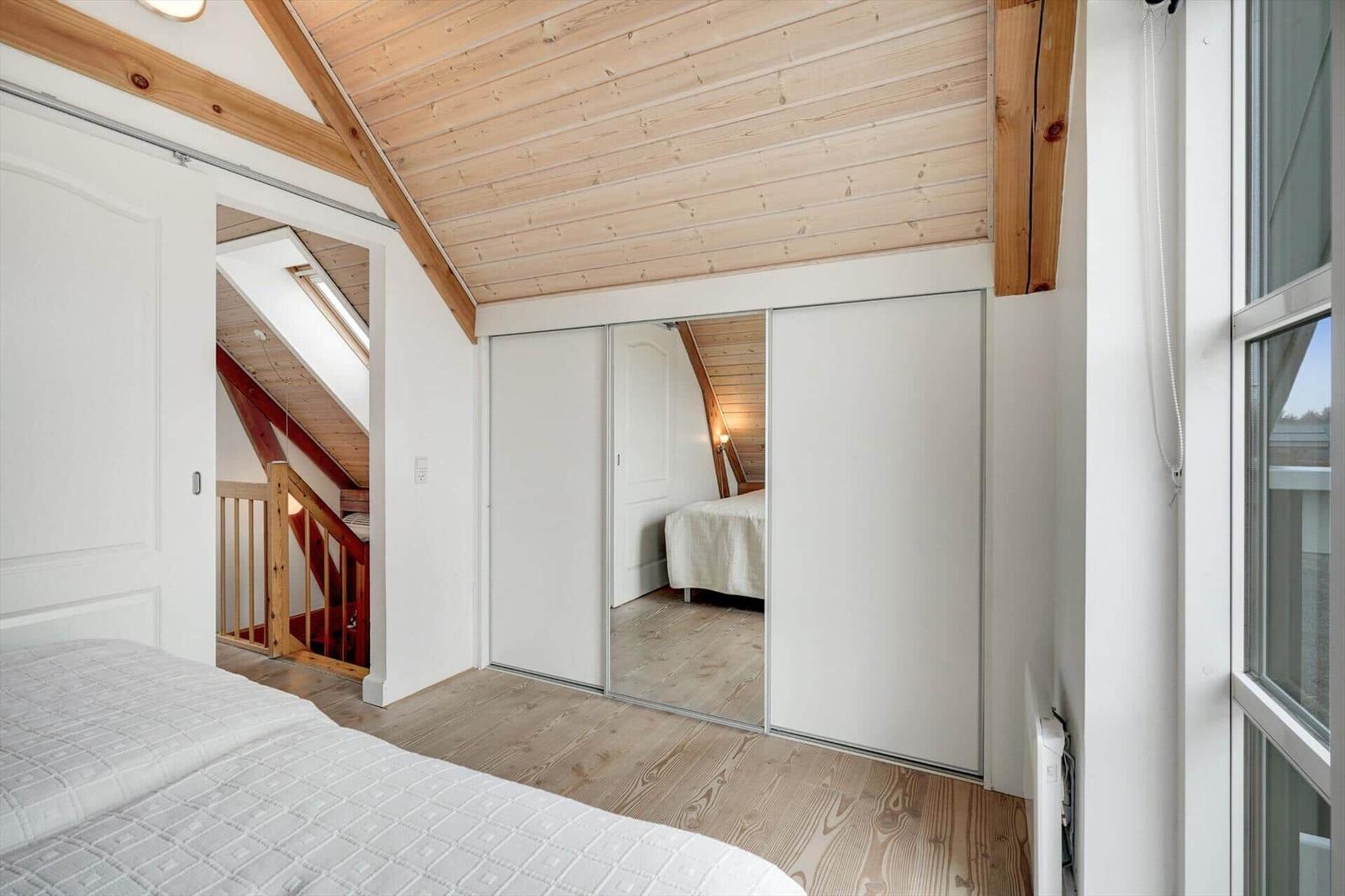 Schlafzimmer mit Holzboden, Spiegelschrank und Dachschrägen. Blick auf Treppenhaus.