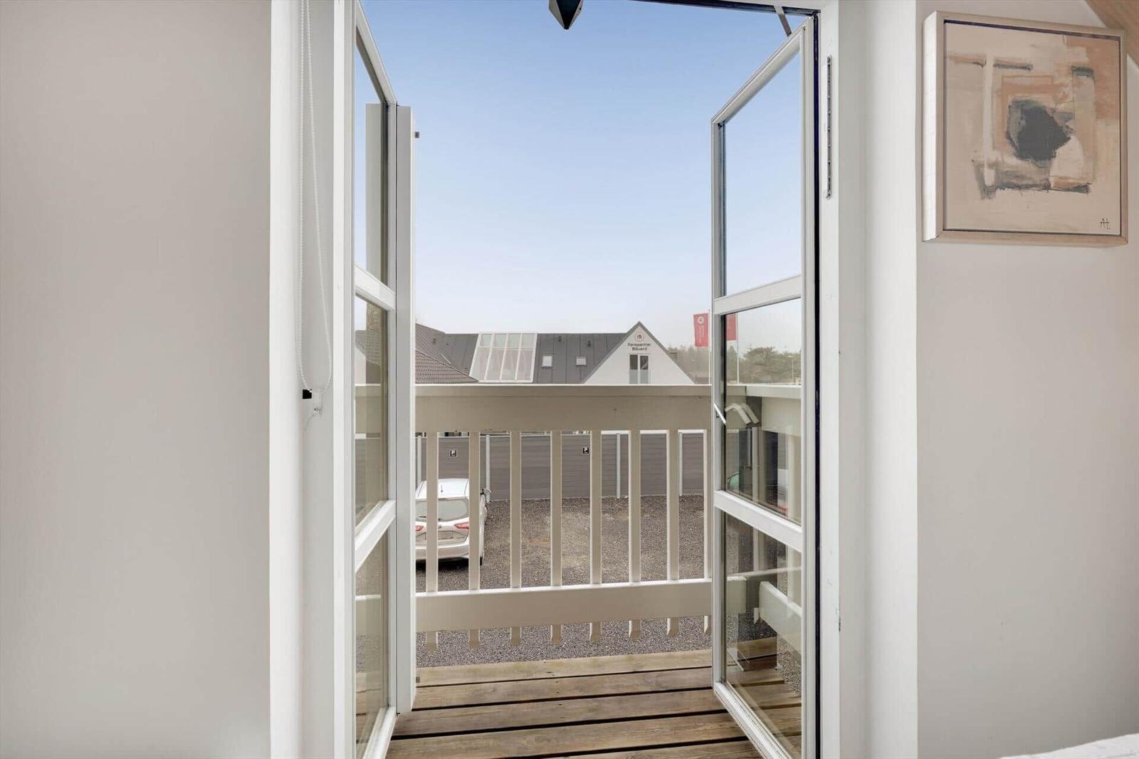 Durch offene Tür zum Balkon mit Holzdielen und Blick auf die Straße.