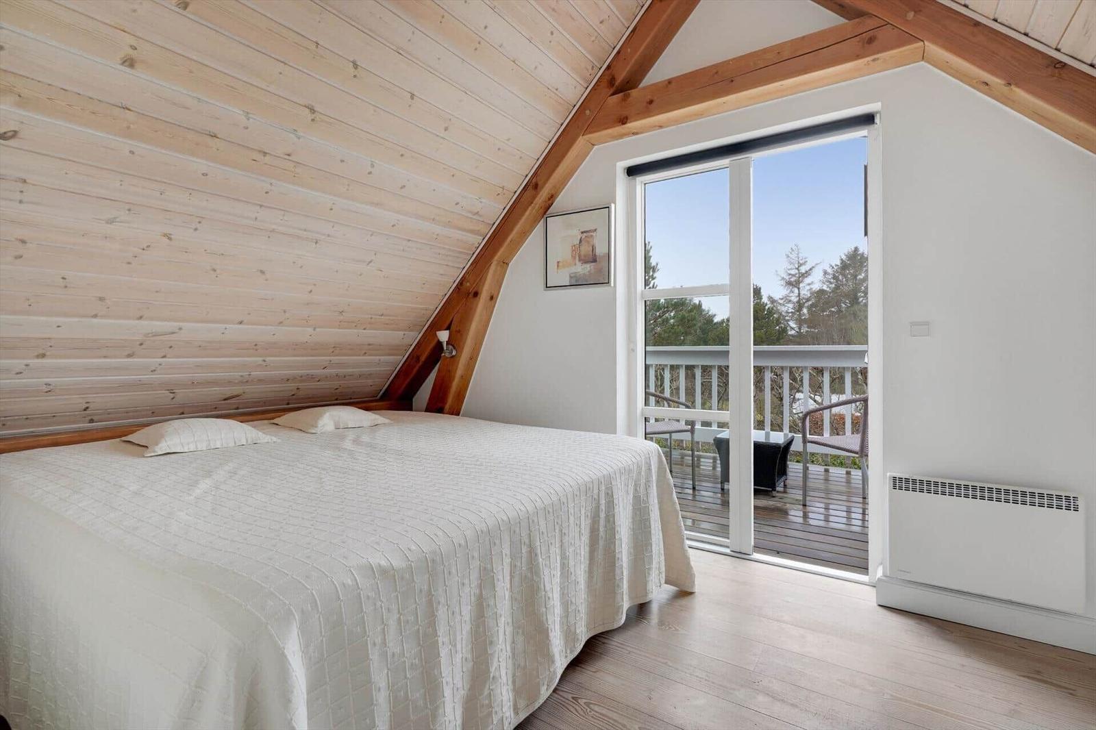 Schlafzimmer mit Balkon und Holzwand. Bett mit weißer Bettwäsche.