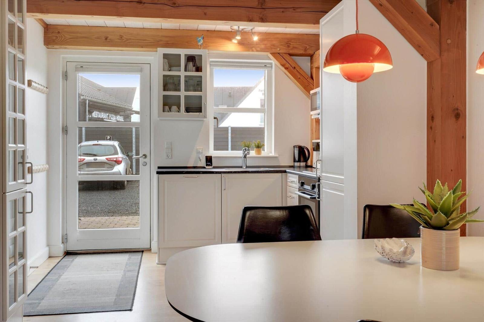 Küche mit Essbereich, weißer Arbeitsfläche, Fenster und Tür zum Außenbereich.