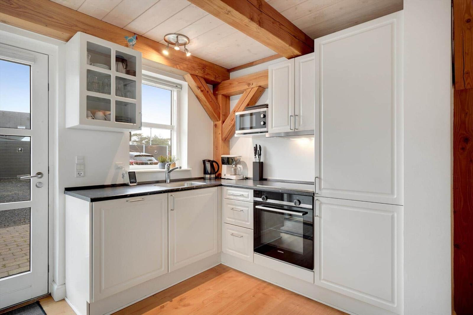 Küche mit weißen Schränken, schwarzer Arbeitsplatte und Holzbalken an der Decke.