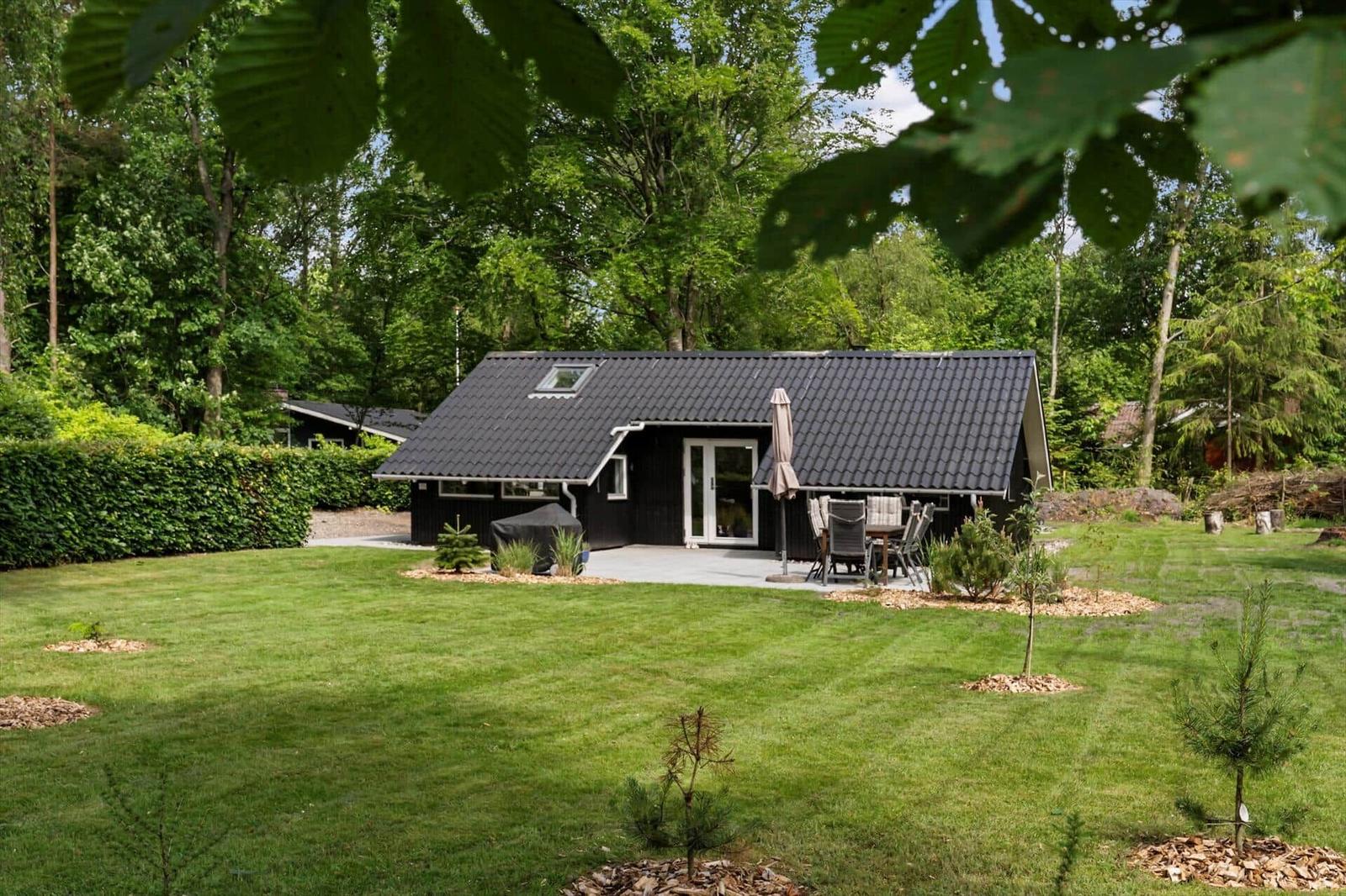 Ein schwarzes Ferienhaus mit Terrasse und Garten inmitten von Bäumen.