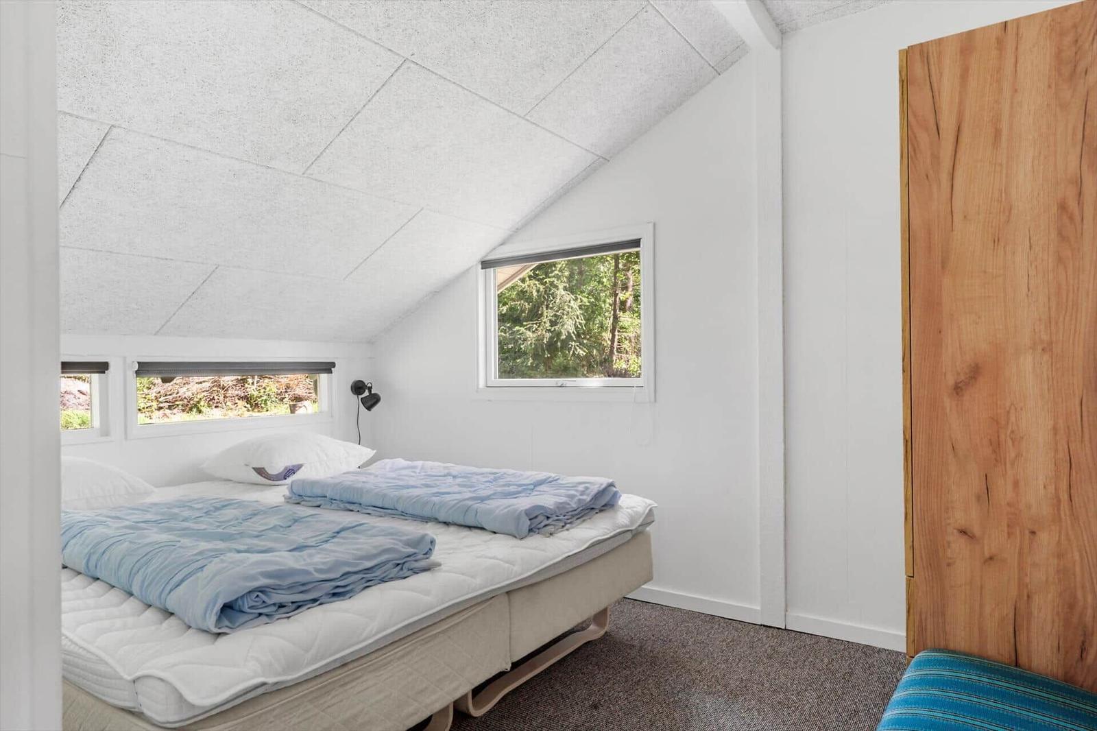 Schlafzimmer mit Doppelbett, Holzwand und Fensterblick auf Wald.