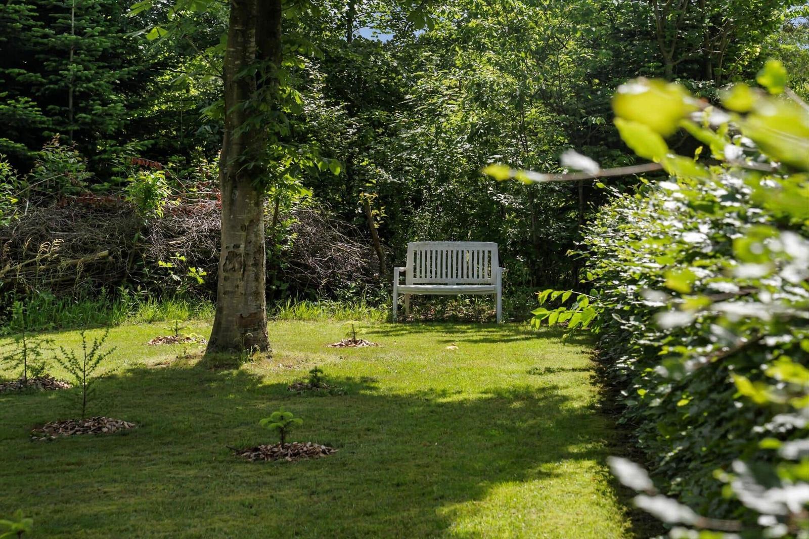 Ein weißer Sitzplatz im grünen Garten unter Bäumen.