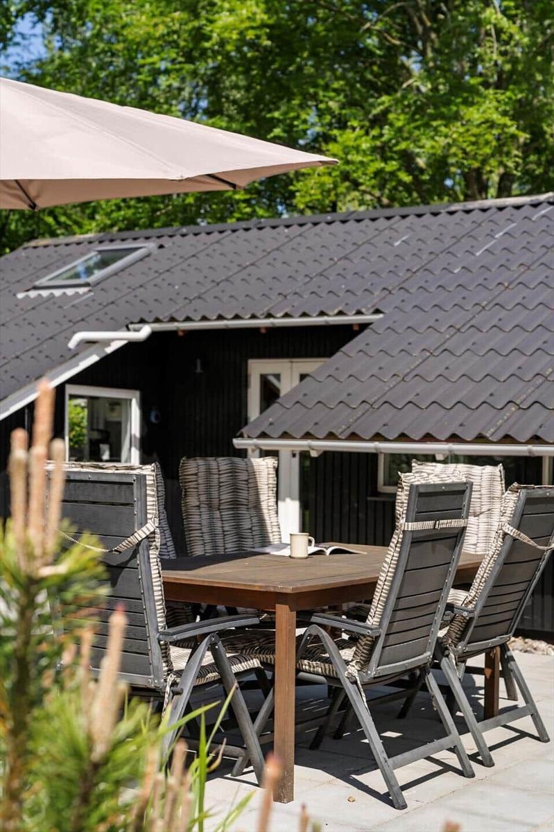 Terrasse mit Tisch, Stühlen und Sonnenschutz vor einem Haus mit dunklem Dach.