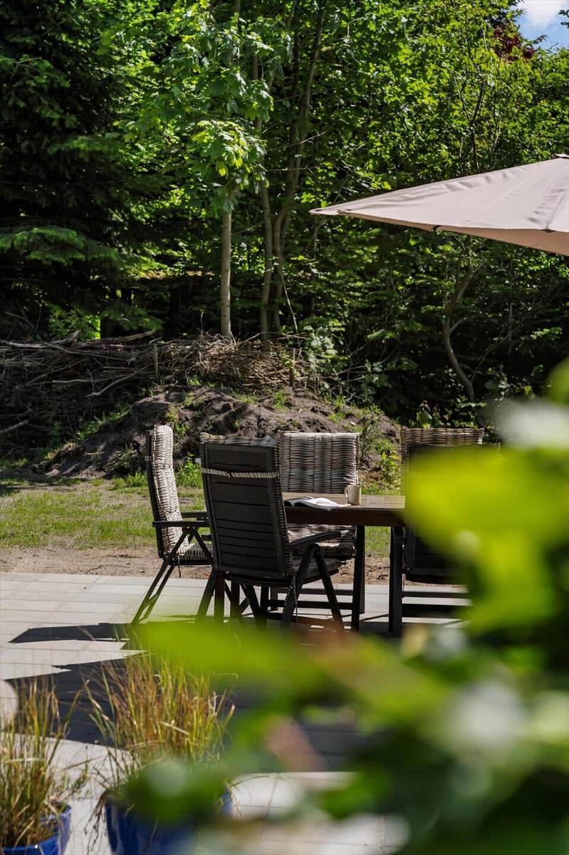 Terrasse mit Tisch, Stühlen und Sonnenschirm im Grünen.