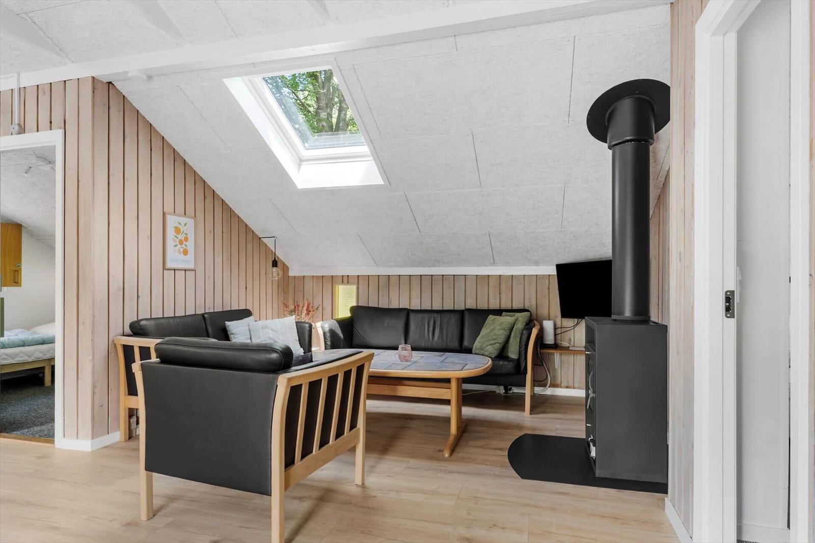 Wohnzimmer mit Sofa, Sessel und Kaminofen unter Dachschrägen.