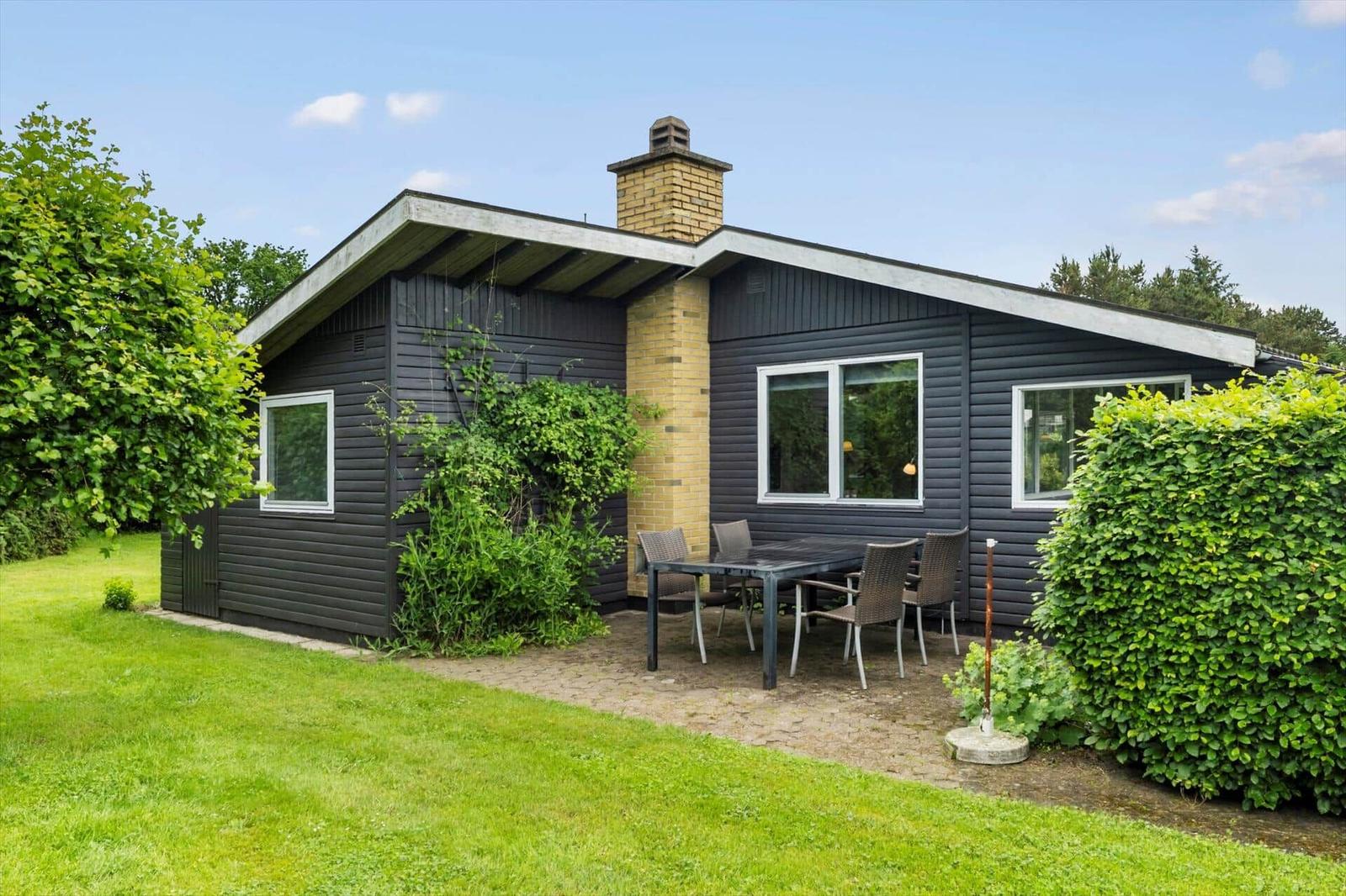 Ein modernes Haus mit Terrasse, Garten und Grillplatz. Fenster und Holzverkleidung sind sichtbar.