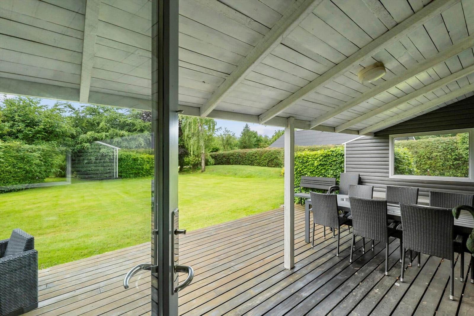 Terrasse mit Tisch und Stühlen, Blick auf grünen Garten und Hecke.