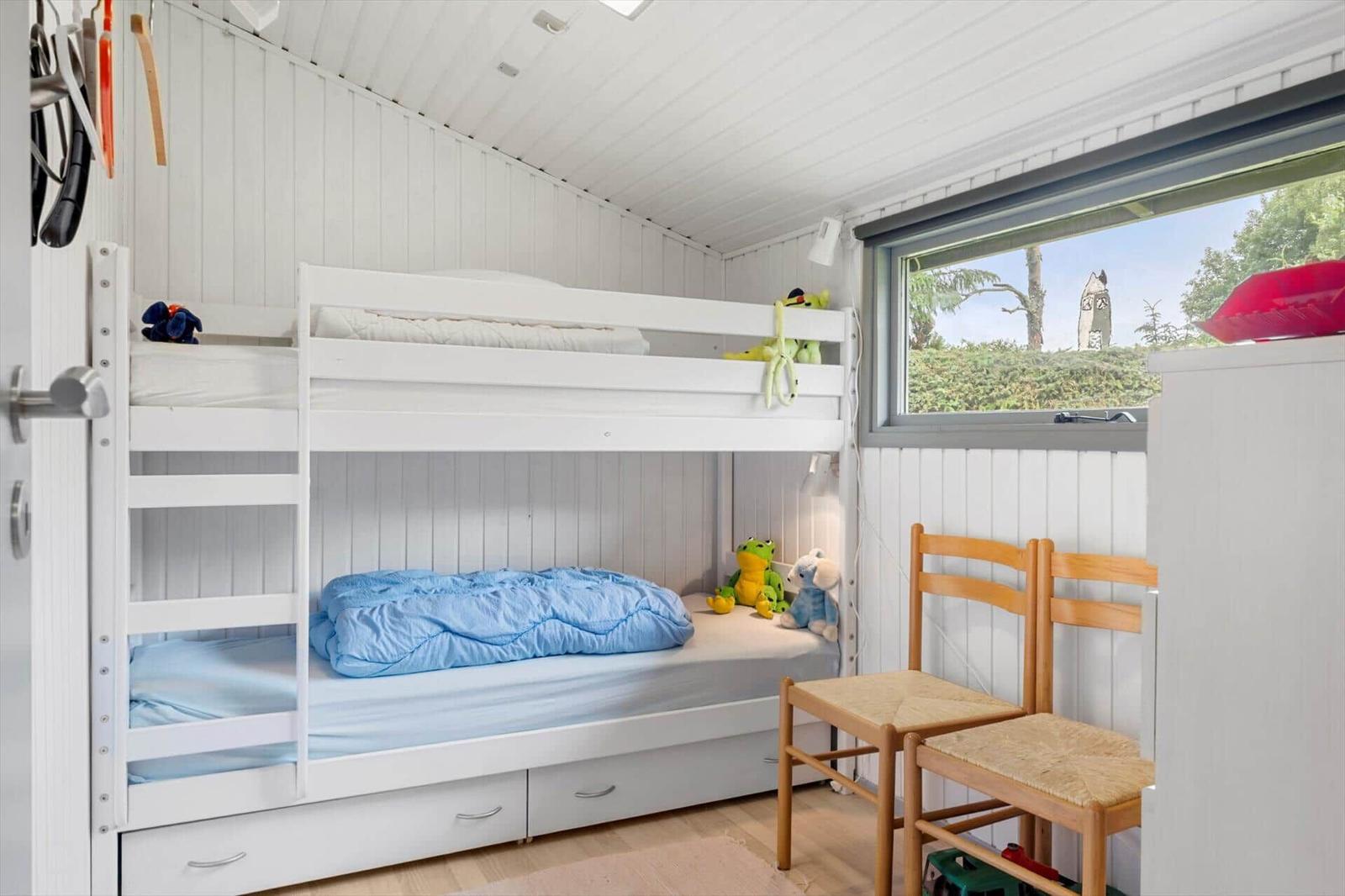 Zimmer mit Doppelstockbett, Fenster und Holzstühlen.