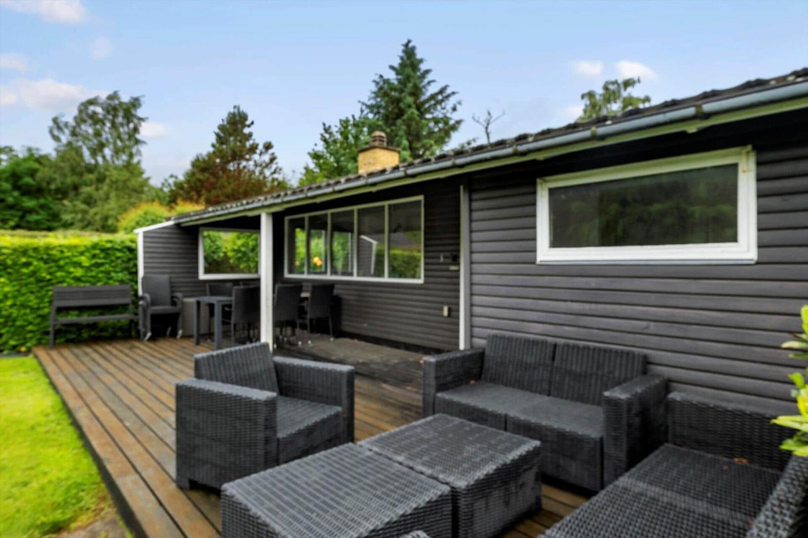 Terrasse mit Sitzgruppe und Tisch. Haus mit dunkler Fassade und Fenstern.