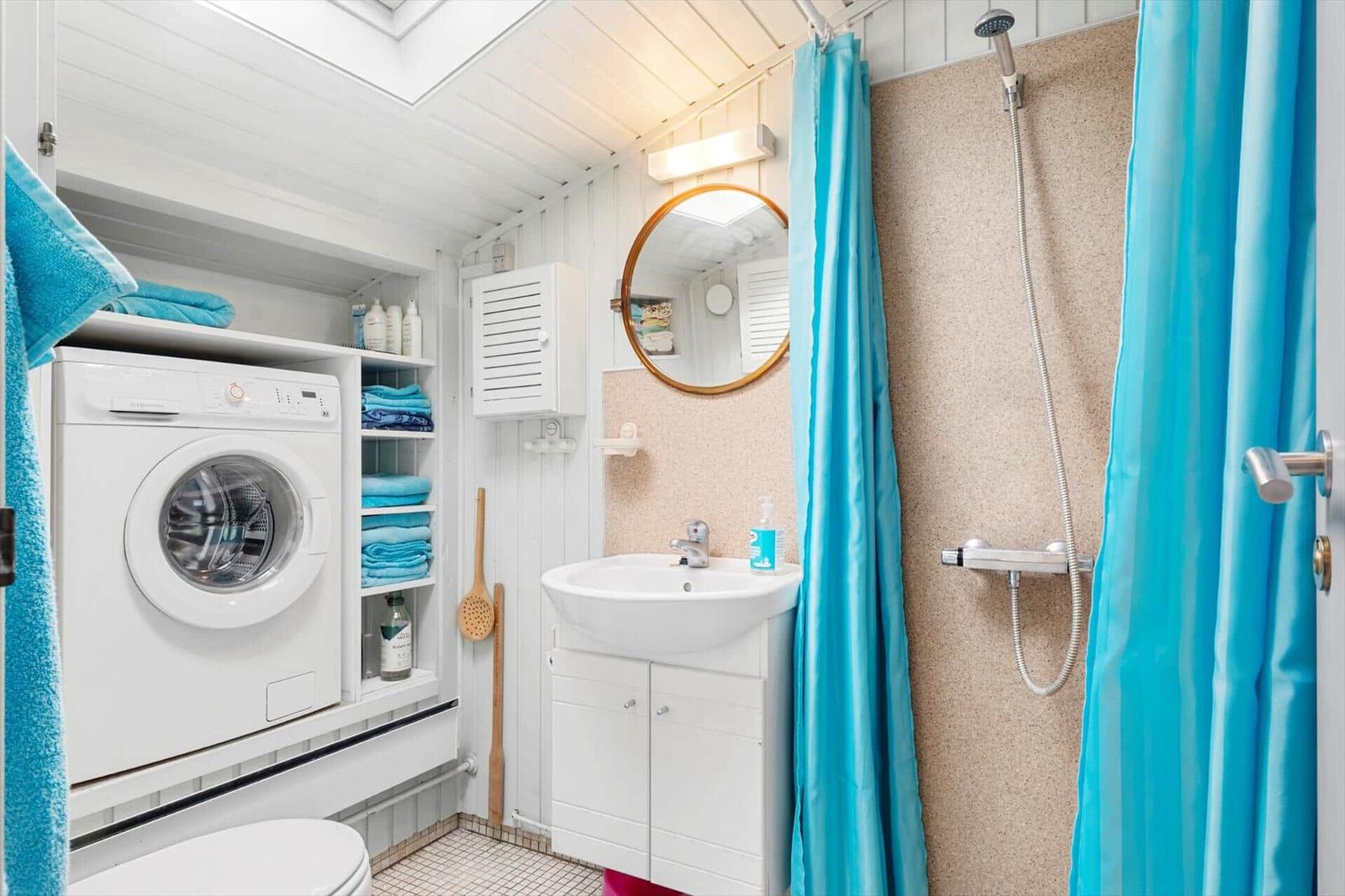 Badezimmer mit Waschmaschine, Dusche und Waschbecken.