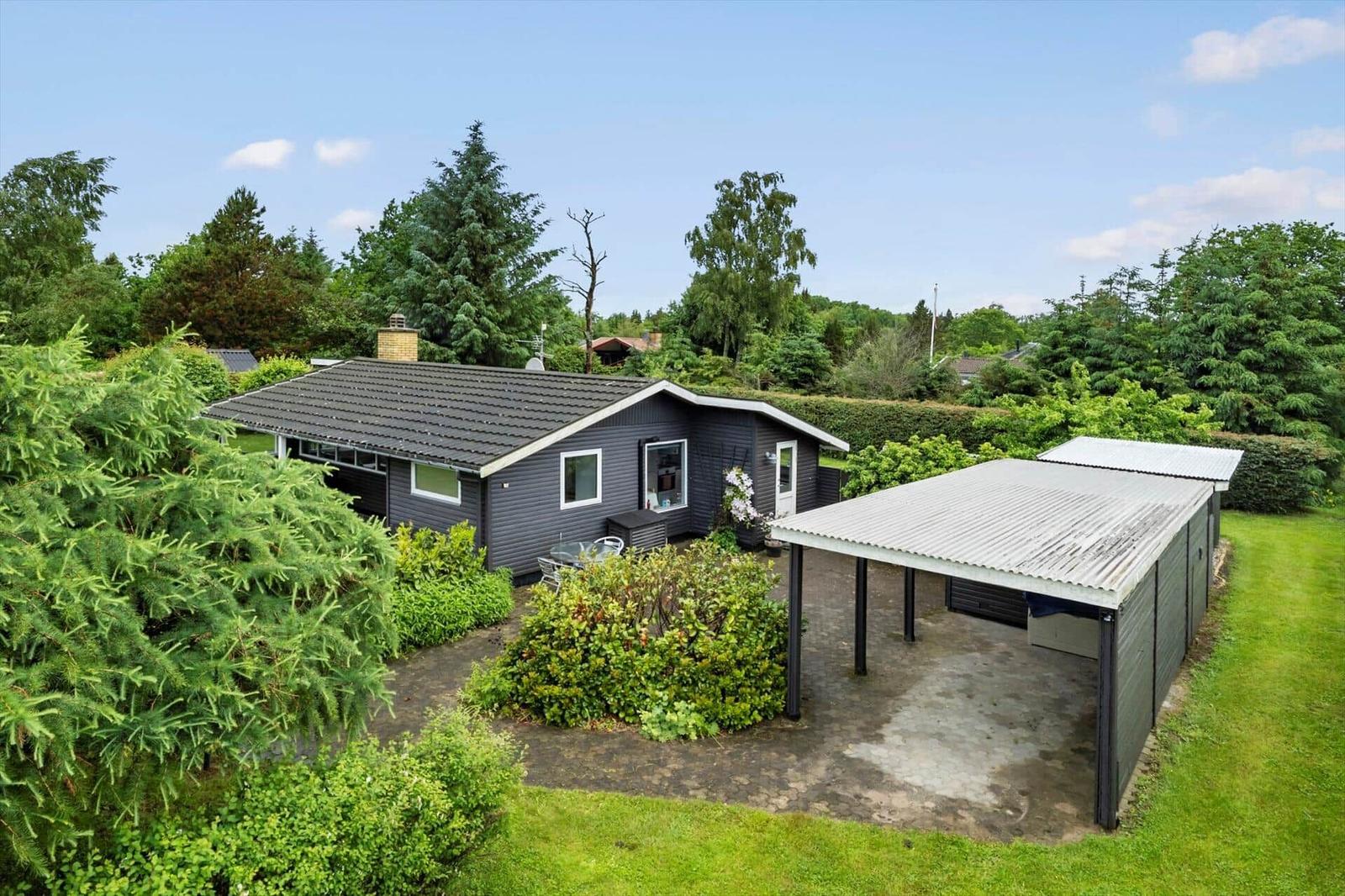 Ein dunkelgrauer Haus mit Terrasse und Carport in grüner Umgebung.