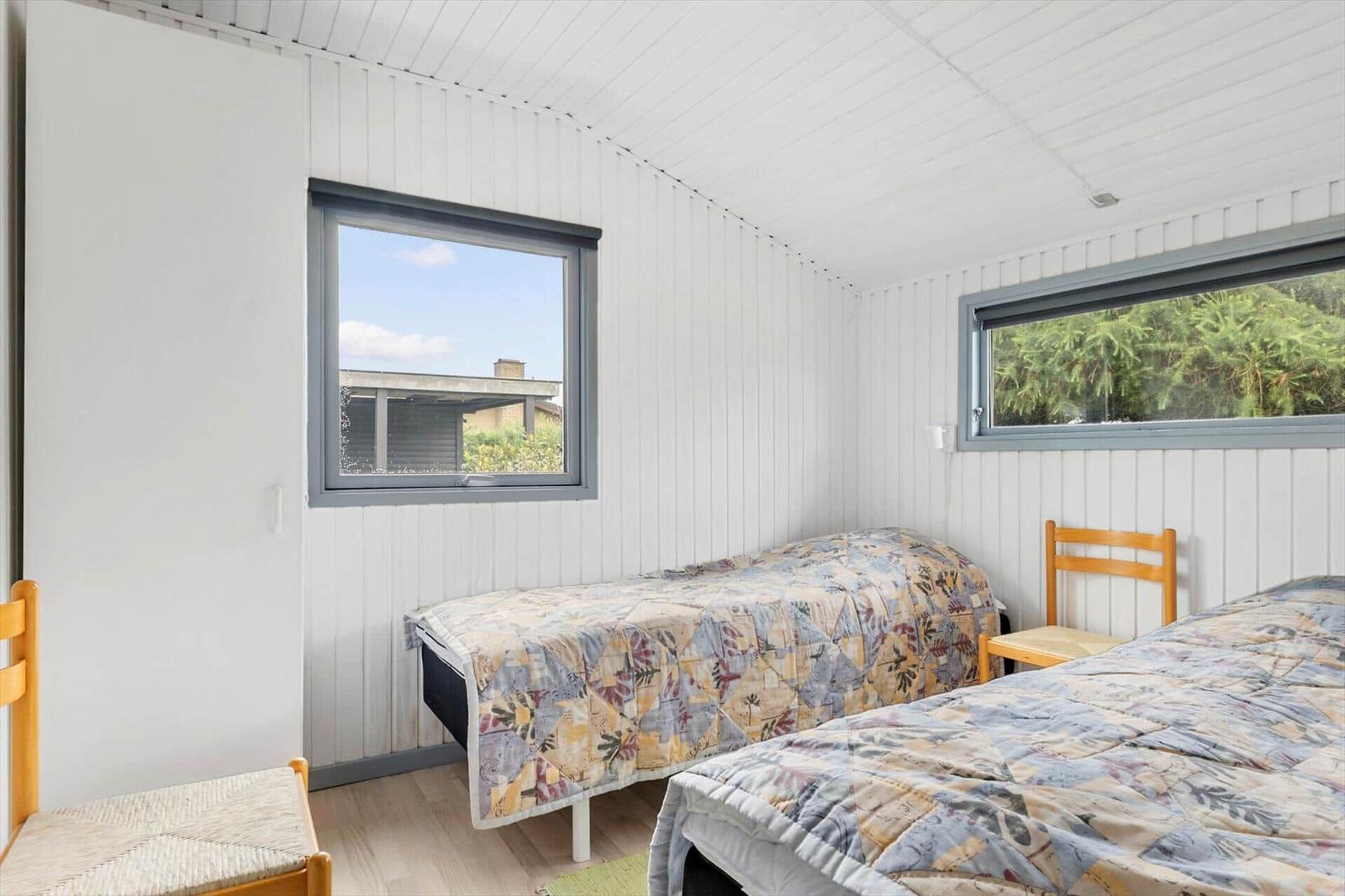 Zwei Betten mit gemusterten Decken, weiße Wände, zwei Fenster mit Blick nach draußen.