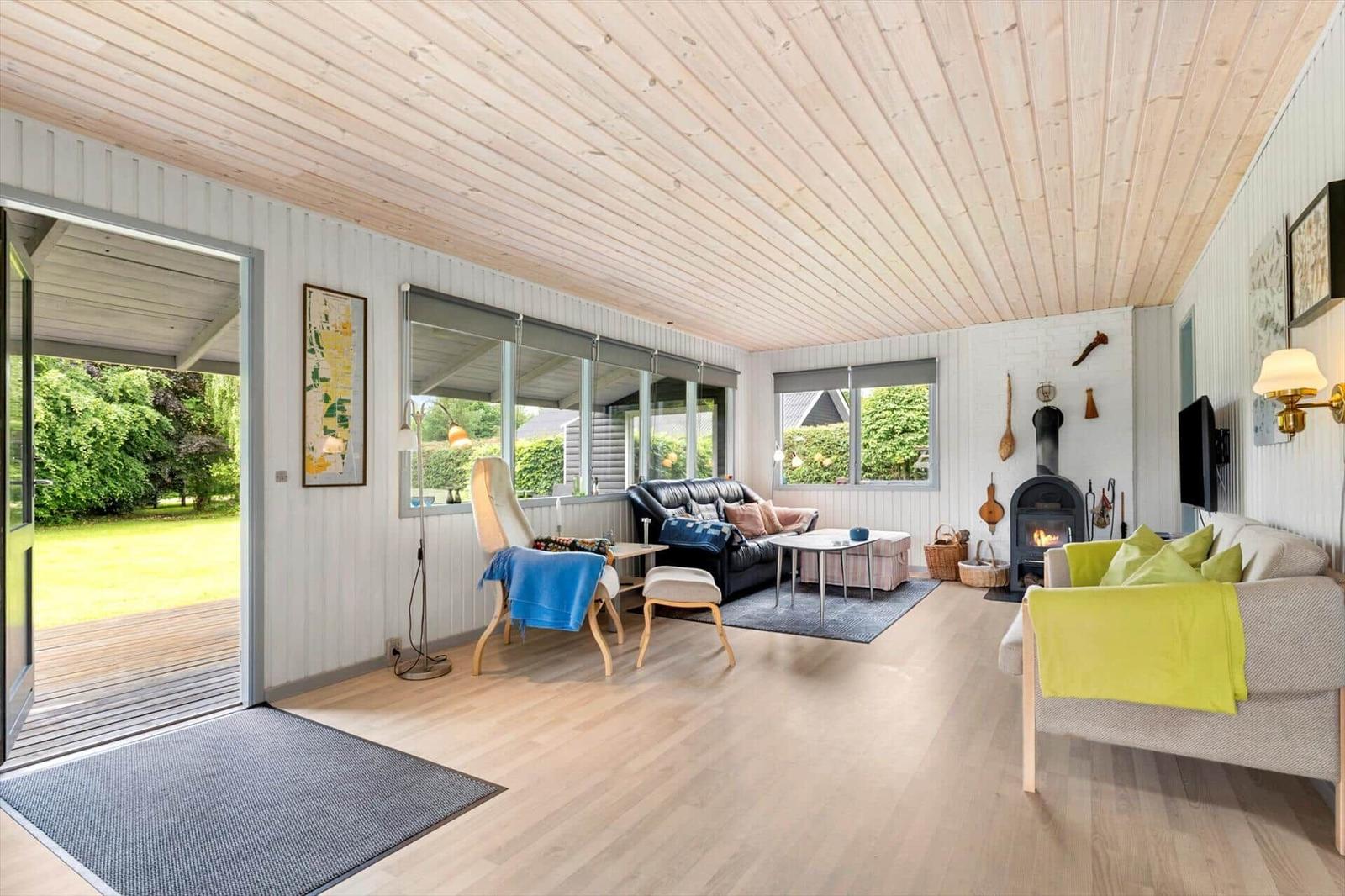 Wohnzimmer mit Holzdecke, Kamin und Blick auf den Garten.