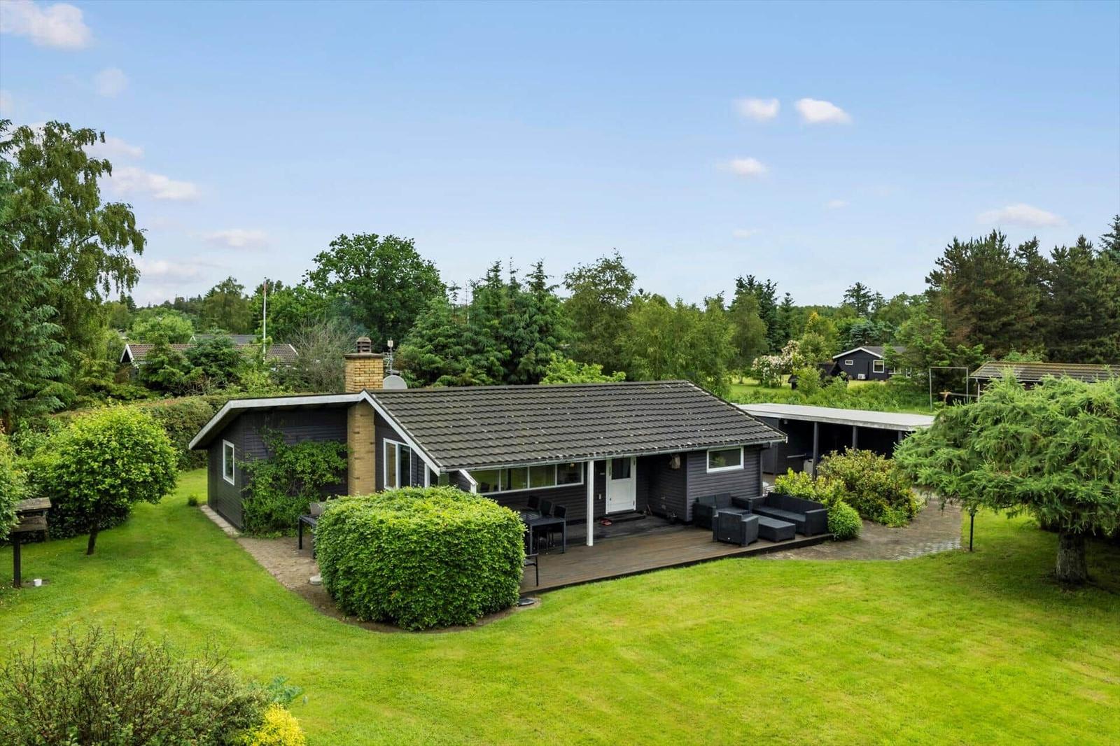 Ein Haus mit Terrasse, Garten und Grillplatz. Umgeben von Bäumen und Gras.
