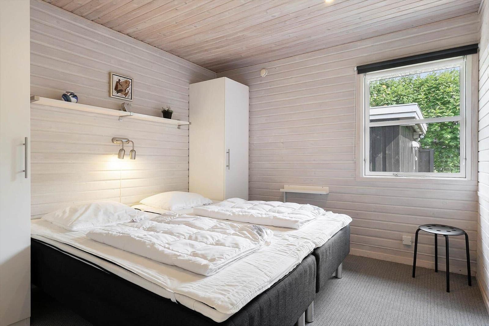 Schlafzimmer mit Doppelbett, weißen Wänden und Fensterblick auf Grün.