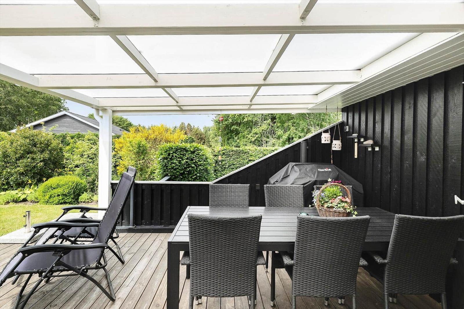 Terrasse mit Tisch, Stühlen und Liegestühlen unter einem weißen Dach.