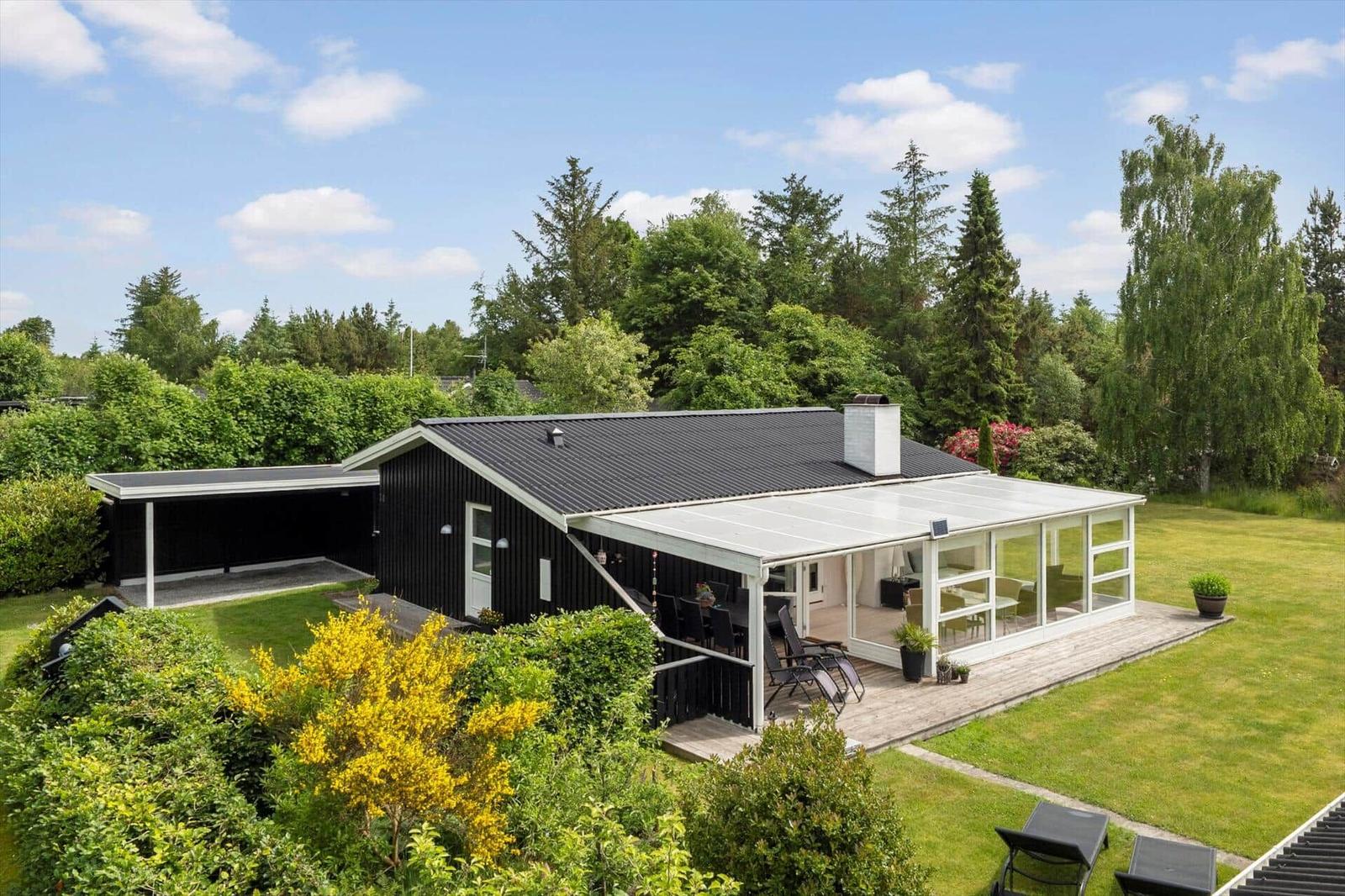 Modernes Haus mit Terrasse und Garten. Umgeben von Bäumen und grünem Rasen.