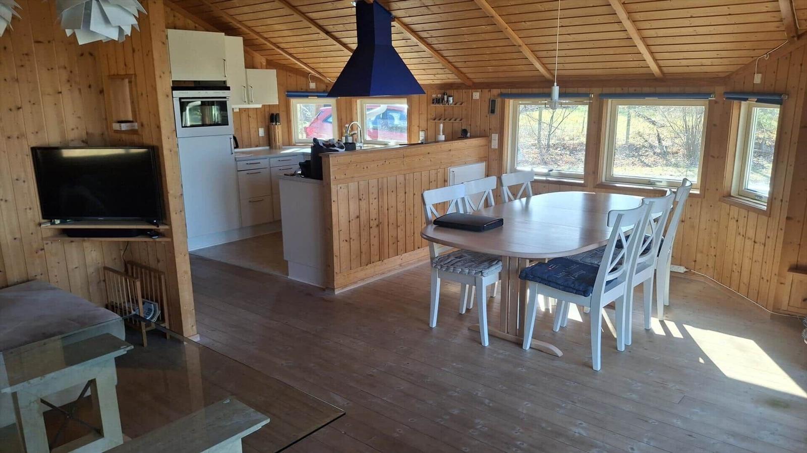 Kitchen and dining area with wooden ceiling and windows. Dining table with chairs and kitchen counter.